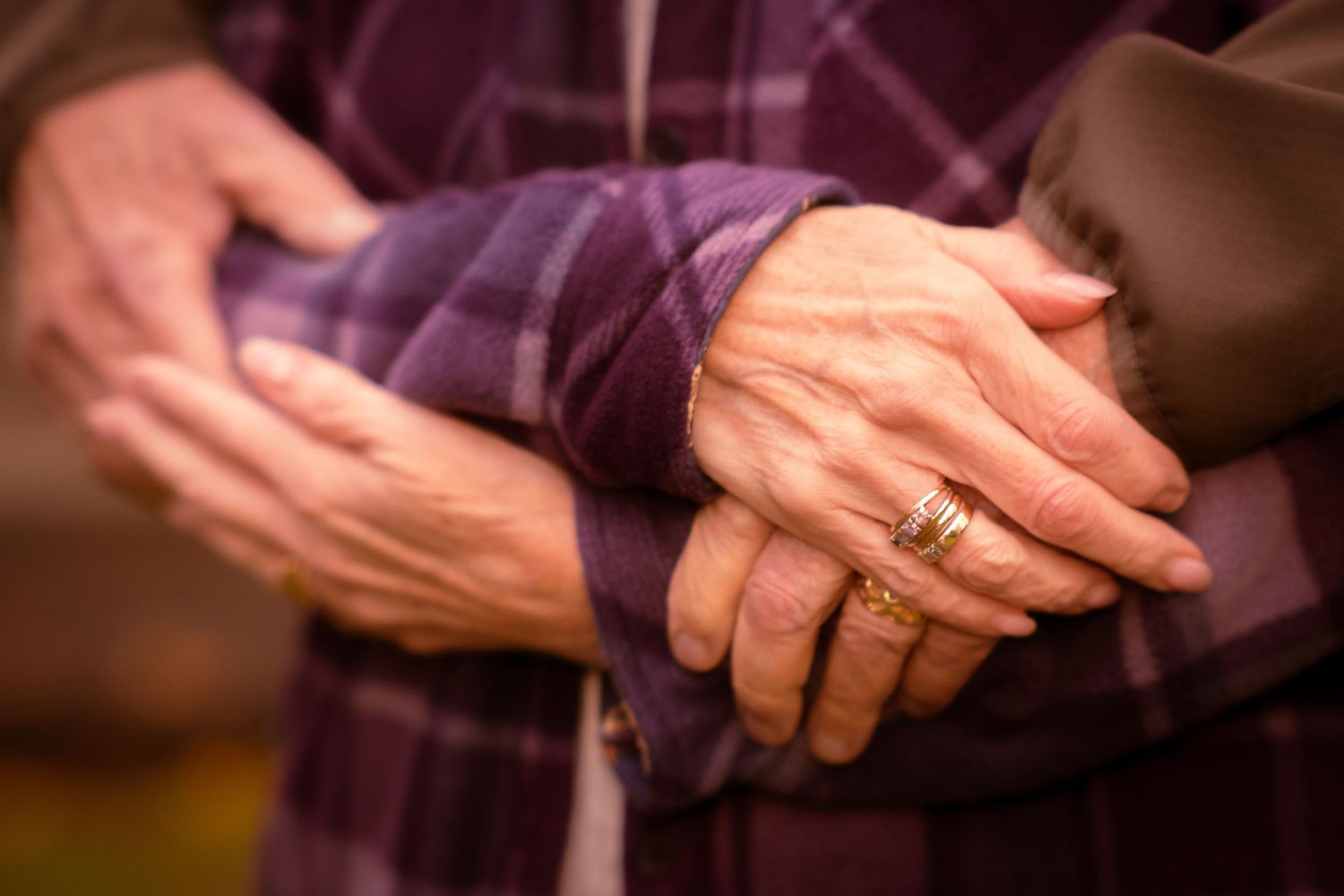 Close-up of senior couple's intertwined hands, one wearing a gold ring, showing tenderness and connection.