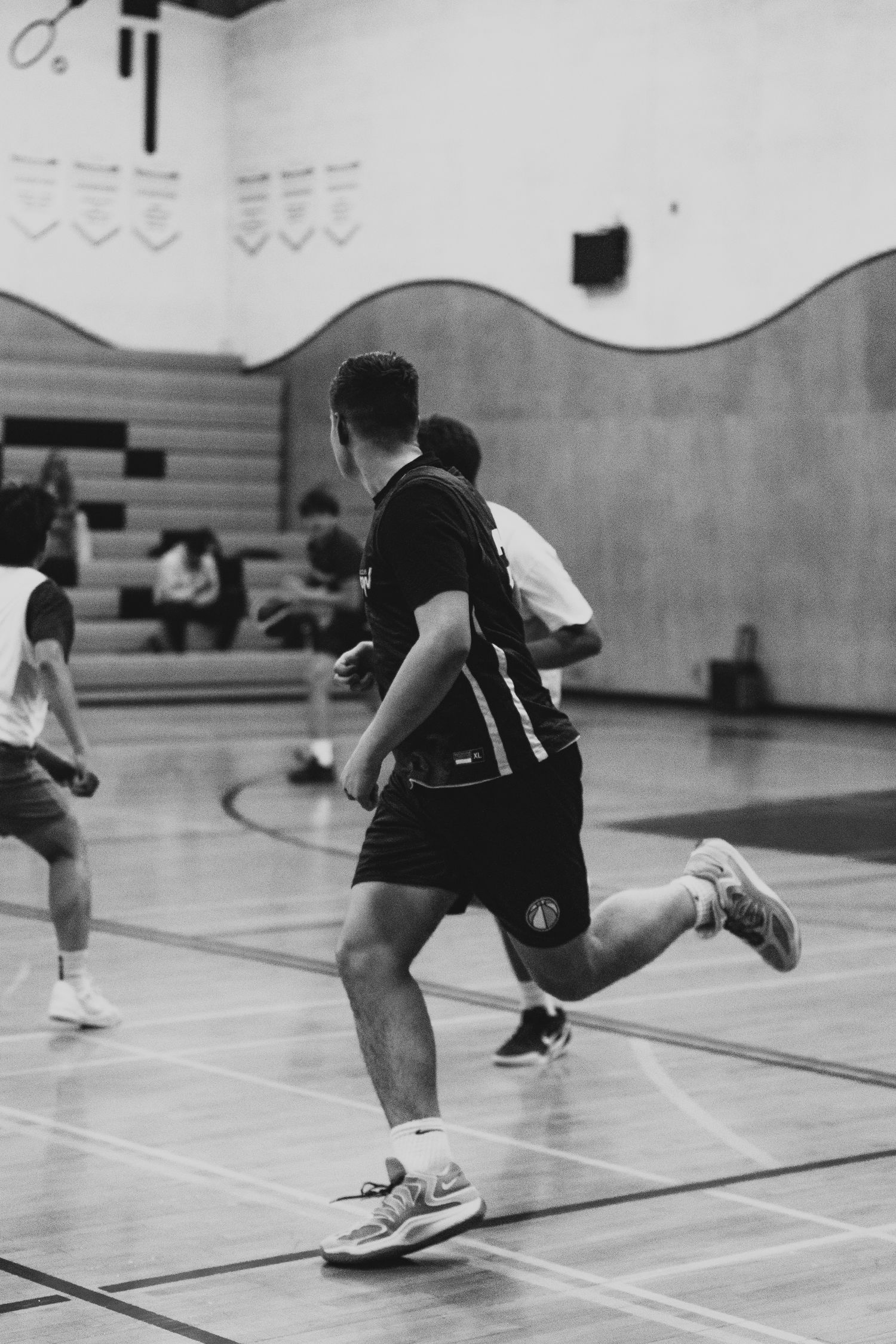 Black and white photo of a basketball player in black uniform running on an indoor court.