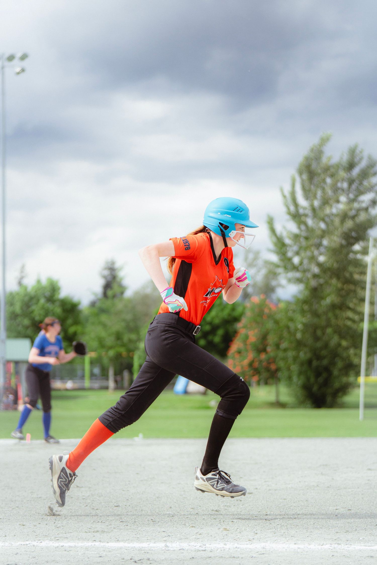 Female softball player in orange uniform sprinting along base path during game.