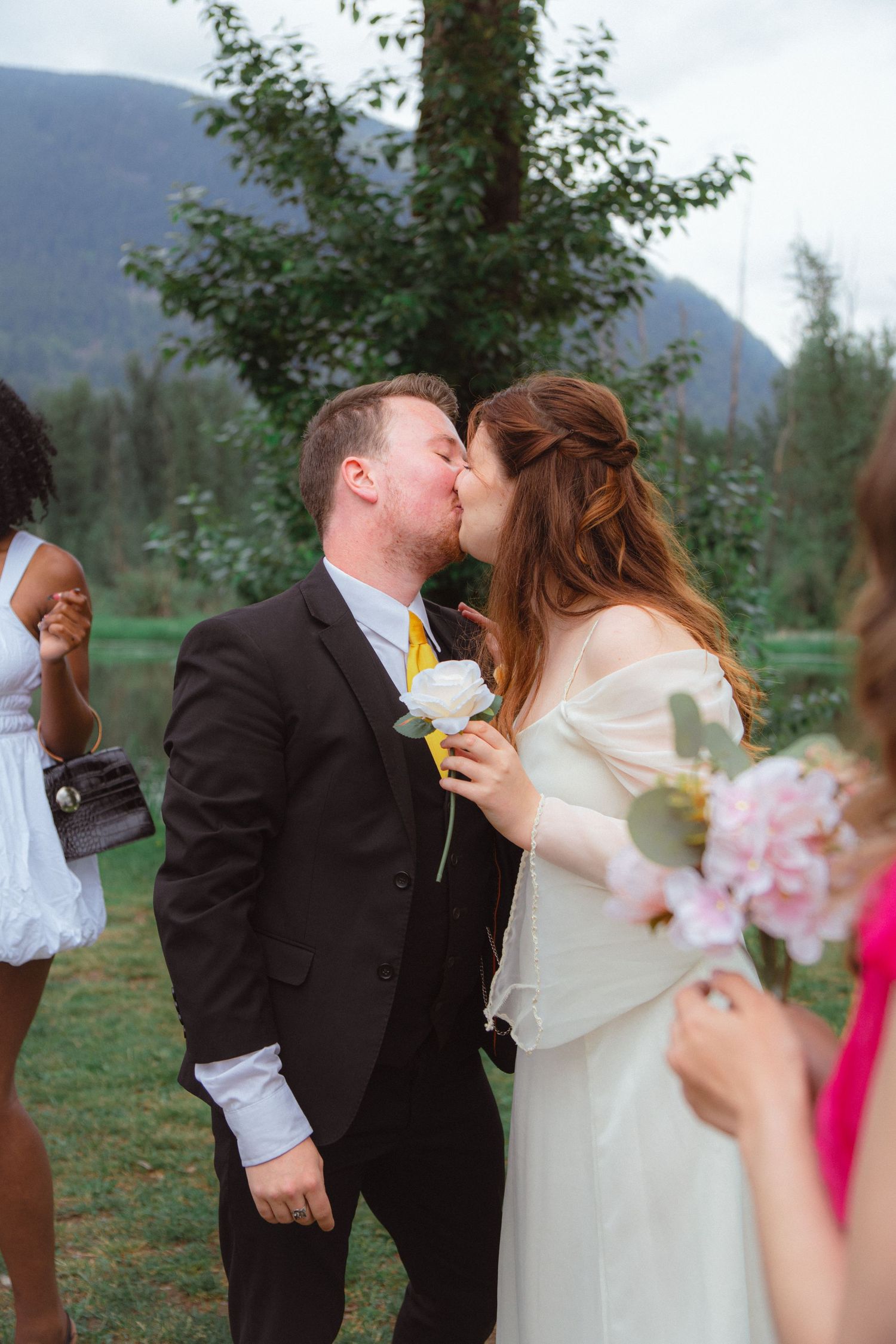 Bride and groom share a first kiss outdoors at a scenic mountain wedding ceremony.