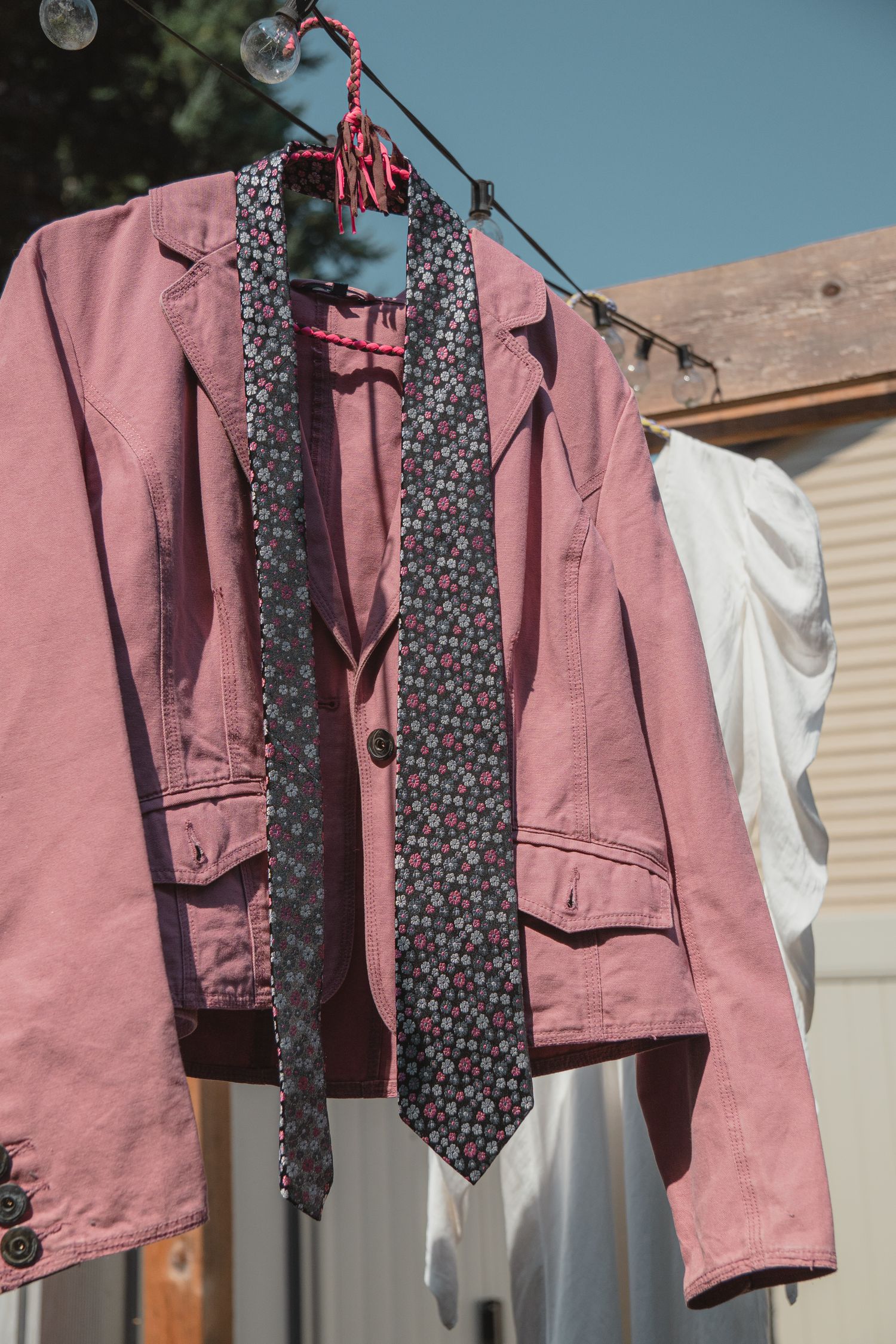 Pink denim jacket with floral tie hanging on clothesline outdoors in sunlight.