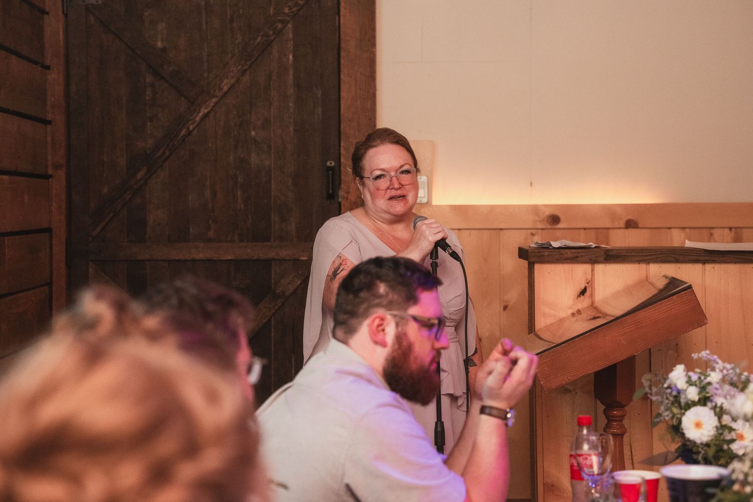 Woman delivers an emotional speech at a podium during a rustic barn wedding reception.