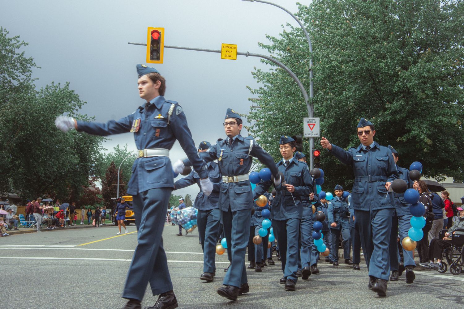 Air cadets in blue uniforms march in formation during a street parade on a cloudy day.