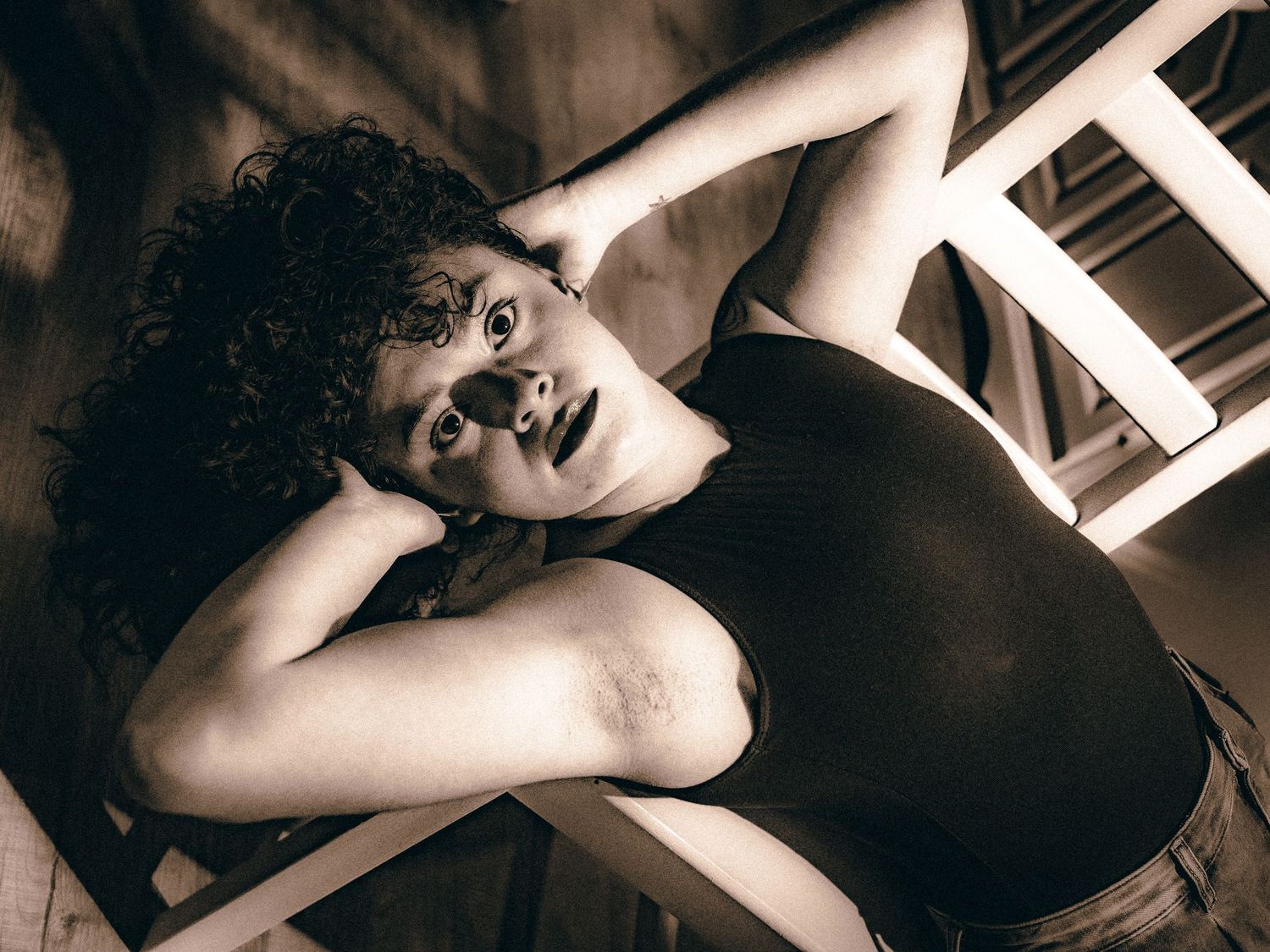 Sepia toned overhead shot of a woman lying back on a chair with expressive wide eyes.