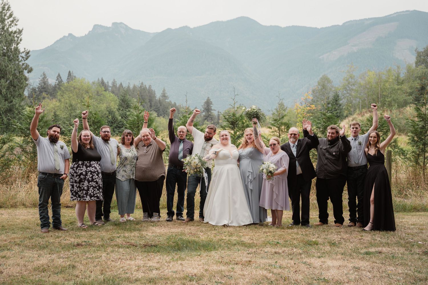 Wedding party celebrates with raised fists in mountain meadow with bride and groom centered.