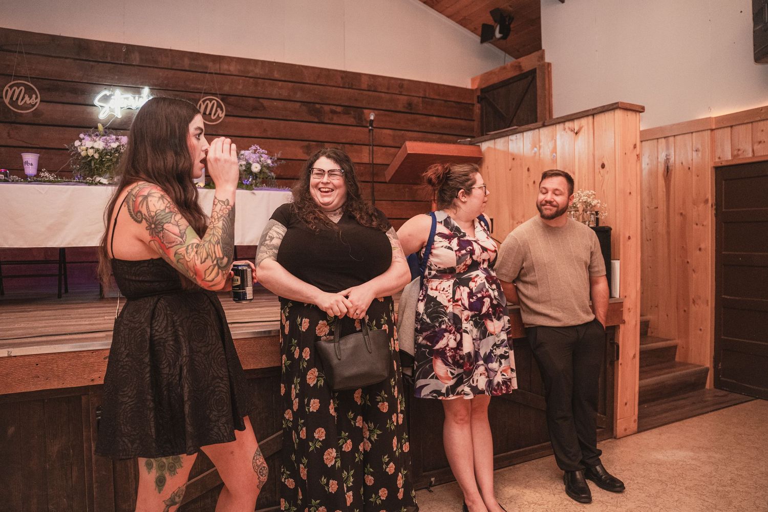 Wedding guests socializing and laughing together in rustic wood-paneled reception venue during wedding celebration.