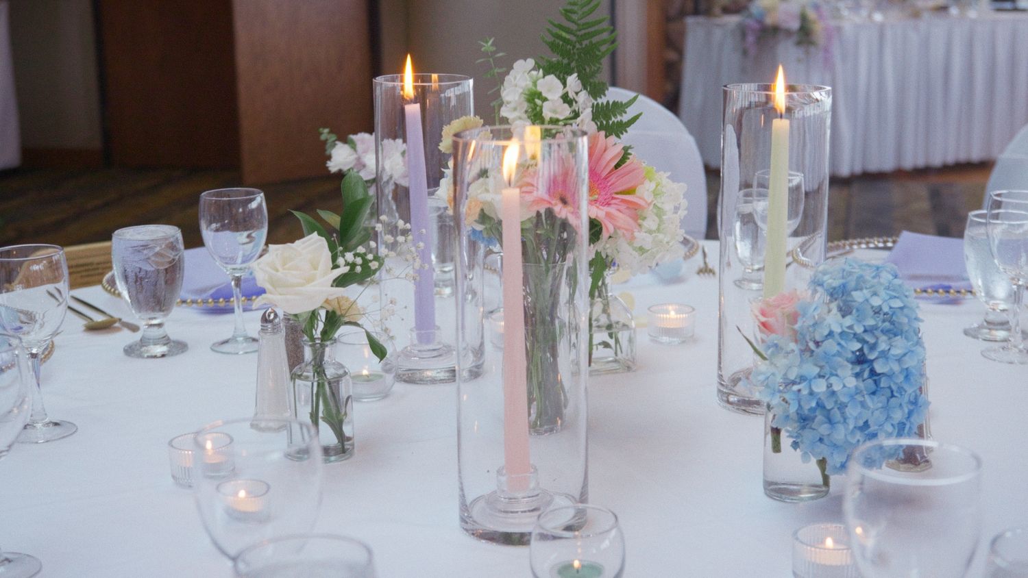 Elegant wedding reception table with pink candles, floral centerpieces, and blue hydrangeas on white linen.