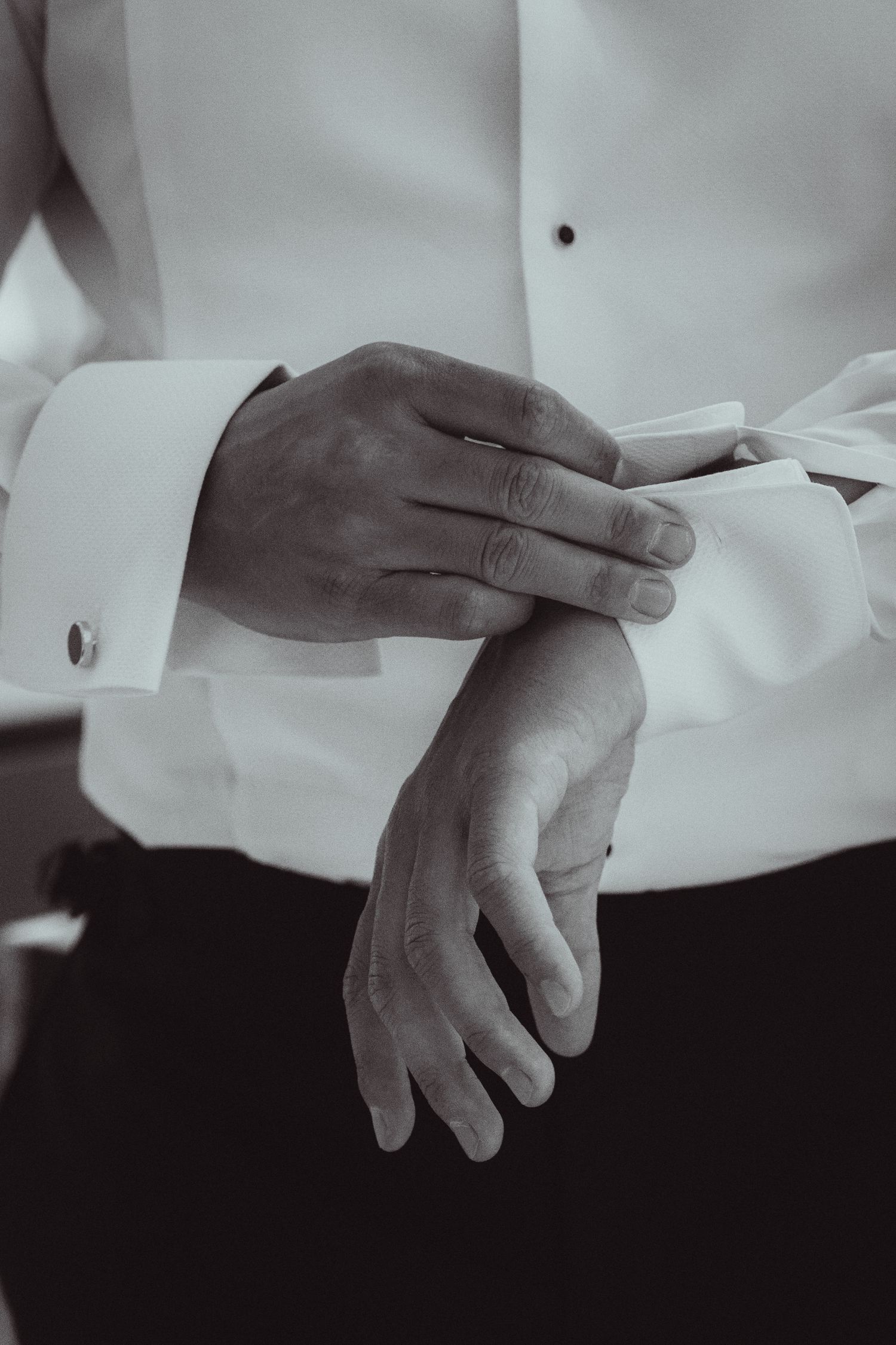 Black and white close-up of groom fastening cufflinks on a white dress shirt before the wedding.