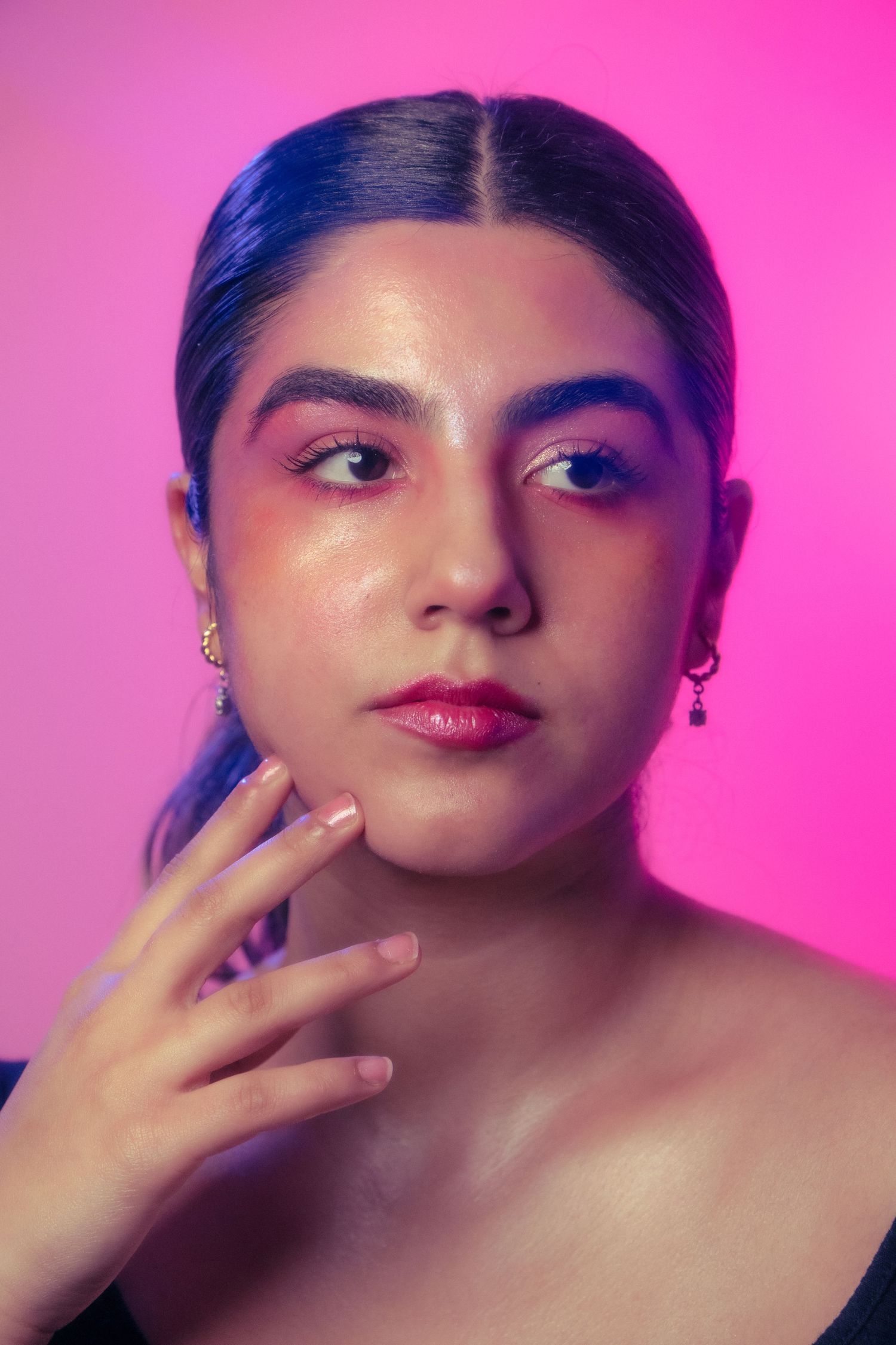 Close-up portrait of young woman with pink eye makeup and red lips touching her face against pink background.