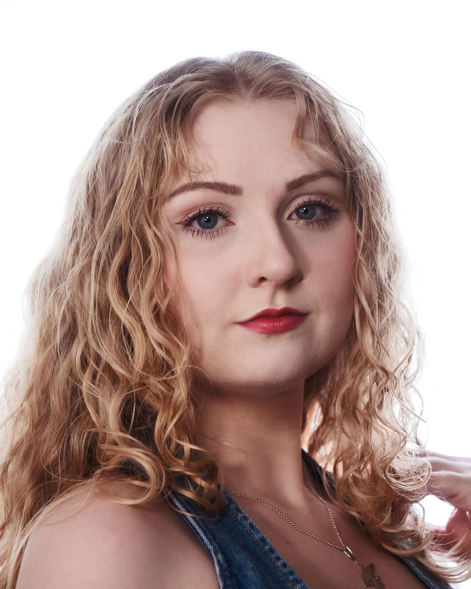 Young woman with curly blonde hair and red lips wearing a denim top, professional headshot on white background.