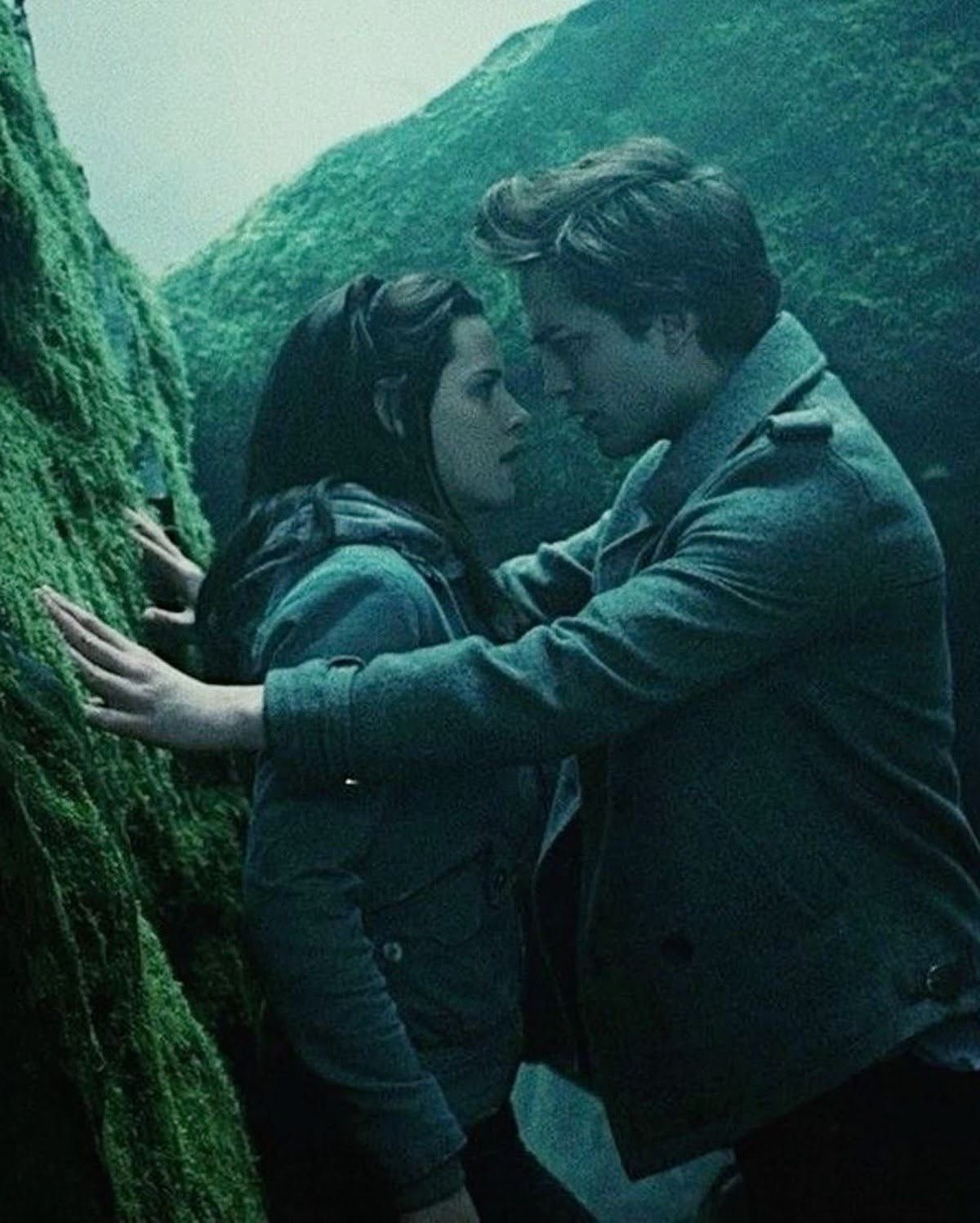 A couple shares an intimate moment pressed against mossy rocks in a misty, dramatic outdoor setting.