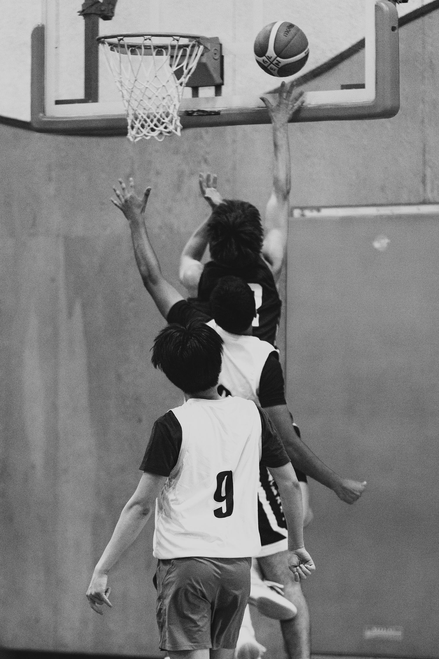Basketball players compete for a layup near the hoop during an indoor game, player 9 visible.