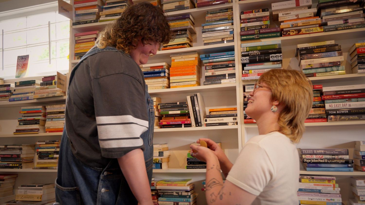 Two people sharing a tender moment in front of a colorful wall of books.