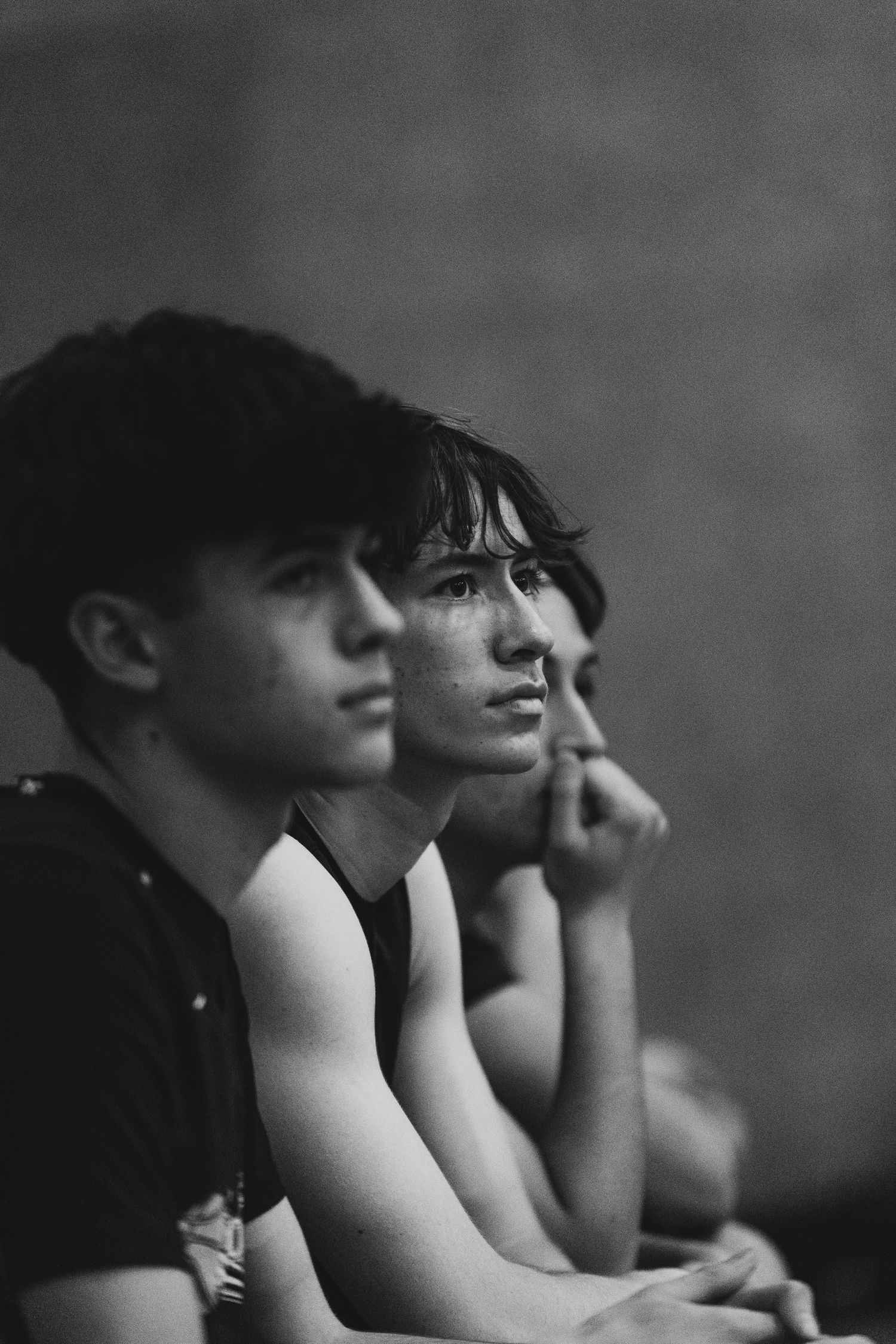 Two young male athletes sit courtside watching a basketball game with focused expressions.