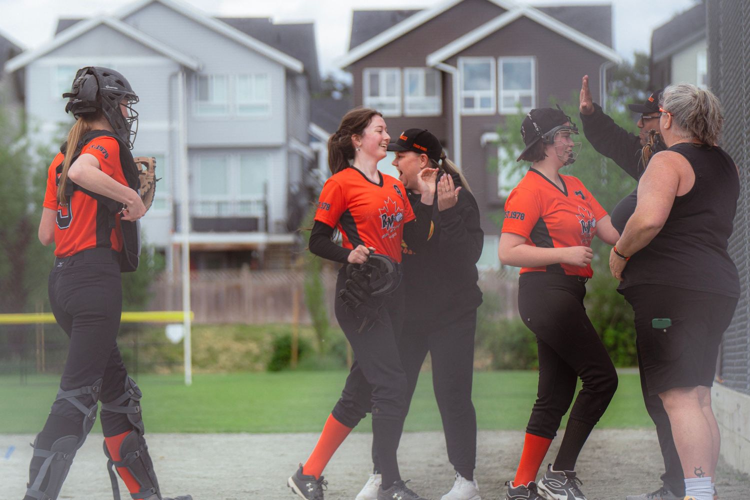 Female softball players in orange uniforms celebrate together with high fives after successful play.
