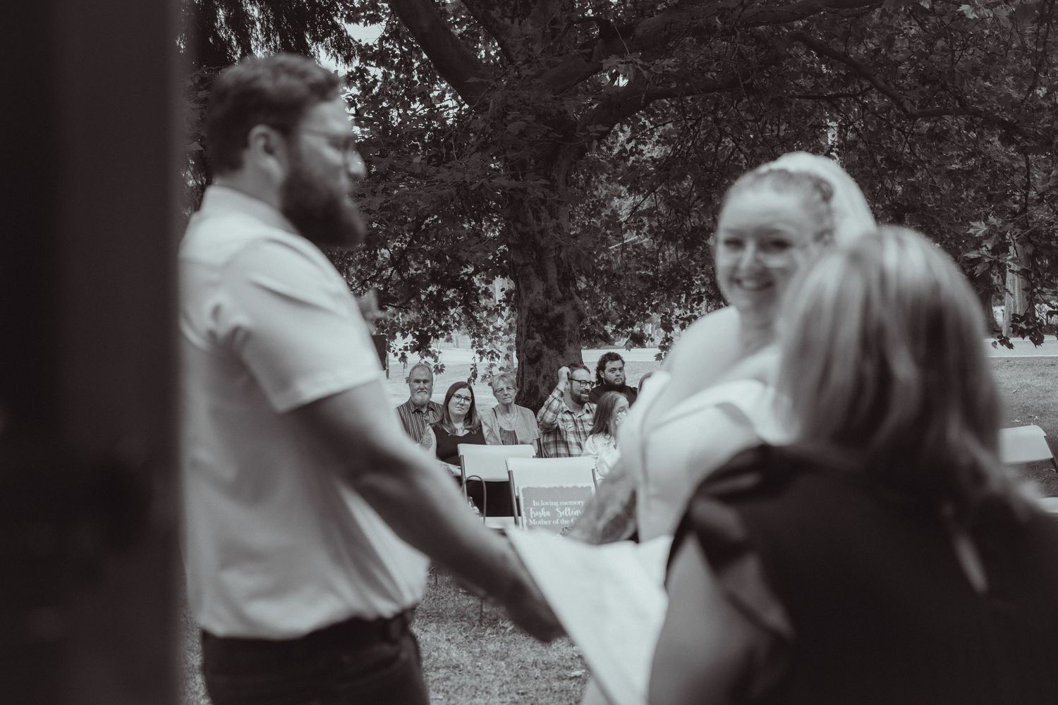 Bride and groom hold hands facing each other during an intimate outdoor wedding ceremony in black and white.