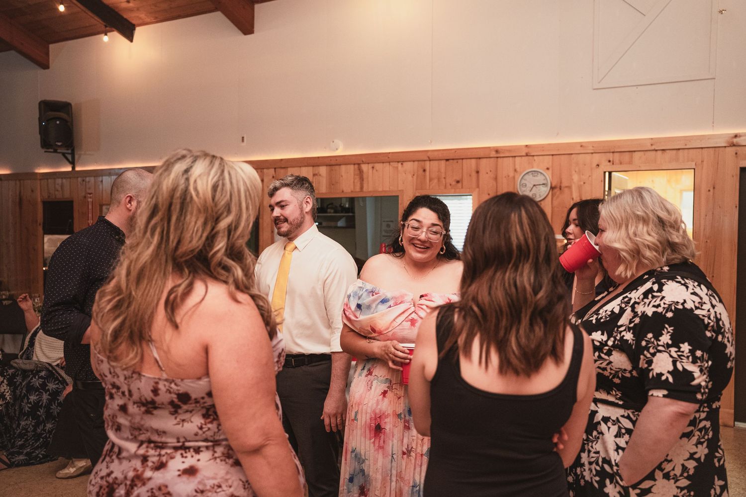 Wedding guests laugh and socialize on the dance floor at a rustic barn reception venue.