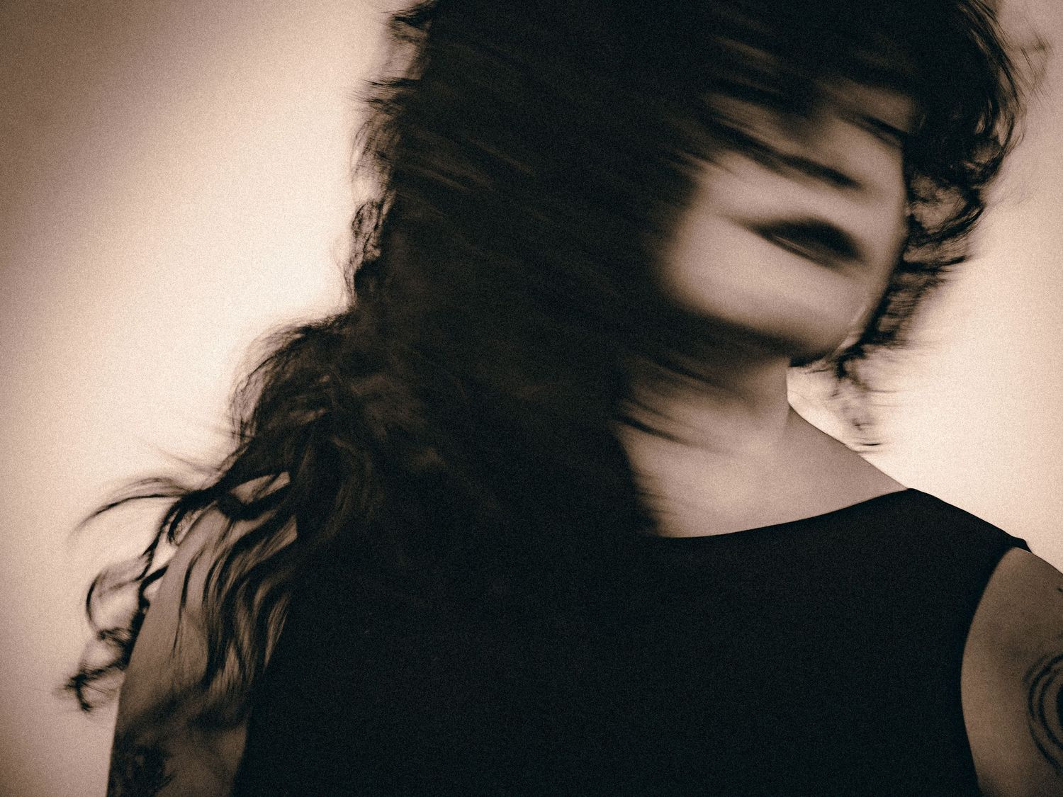 Motion blur portrait of a woman with flowing dark hair obscuring her face in sepia style.