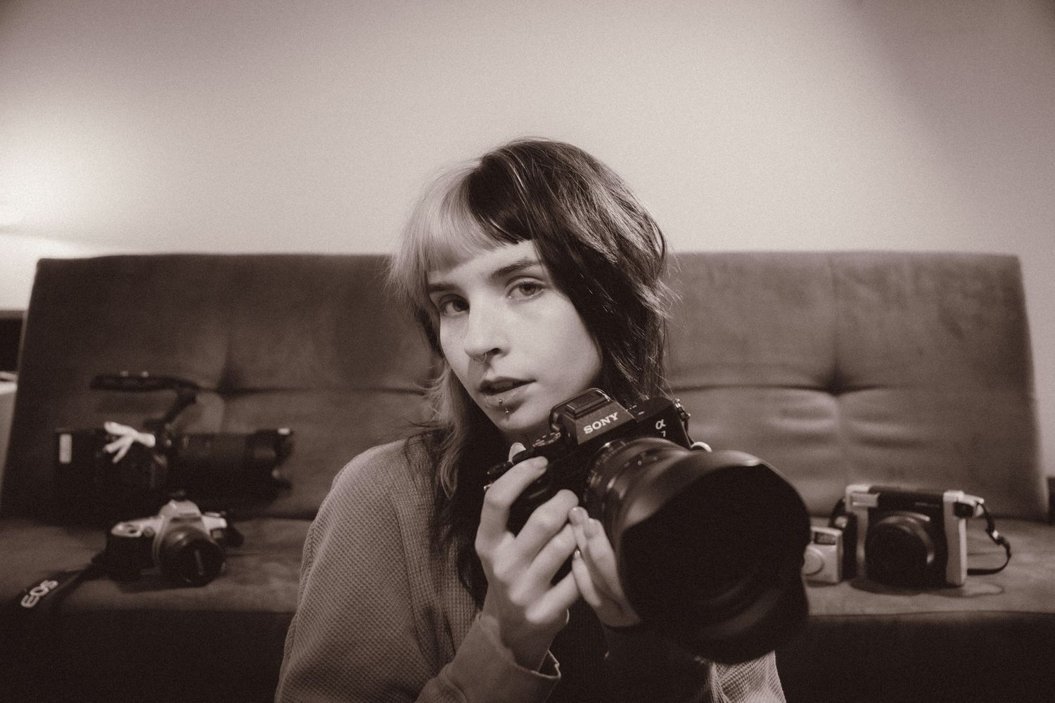 Young person holding a camera with multiple cameras on a couch in a black and white photo.