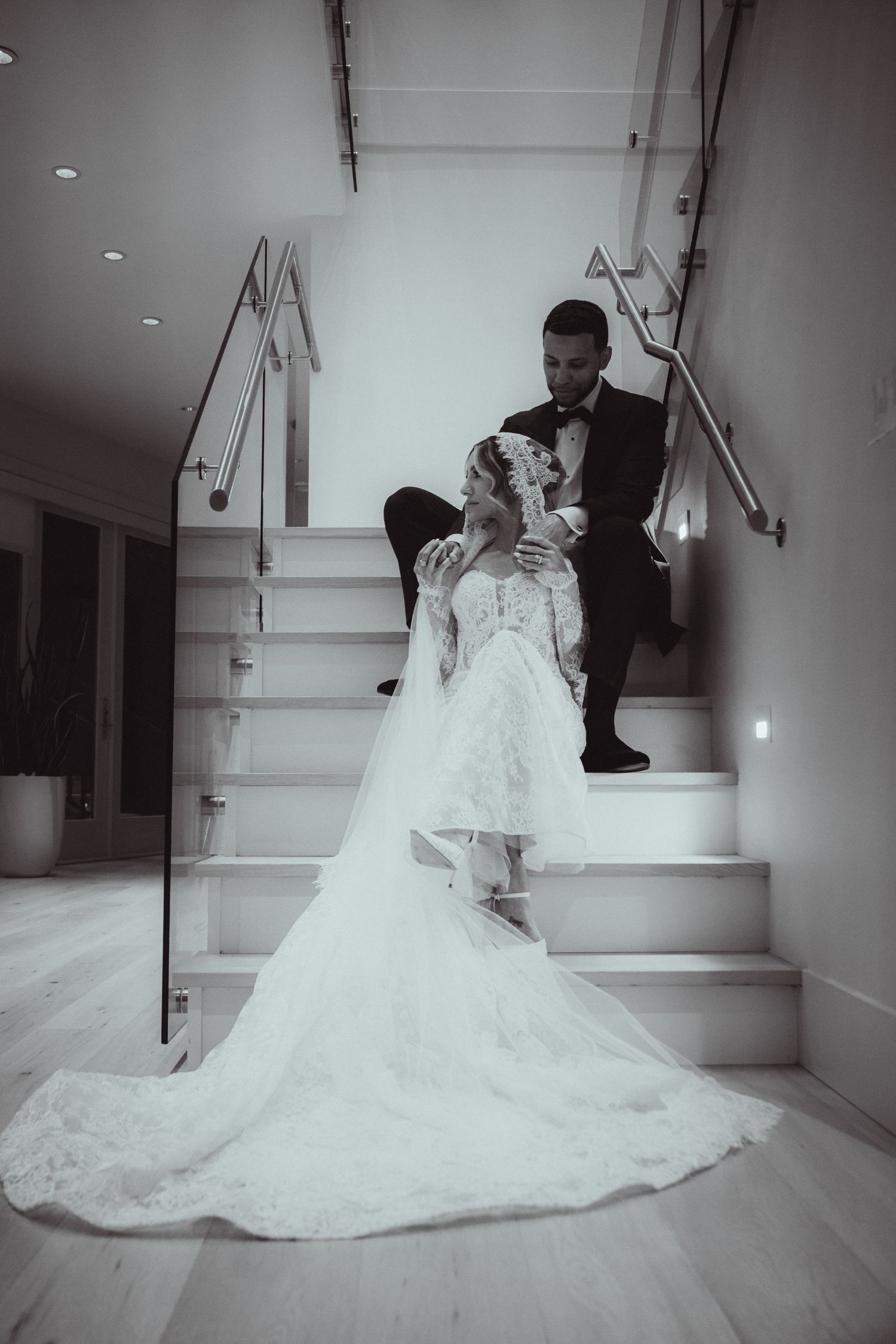 Bride and groom pose romantically on elegant staircase in black and white wedding portrait.