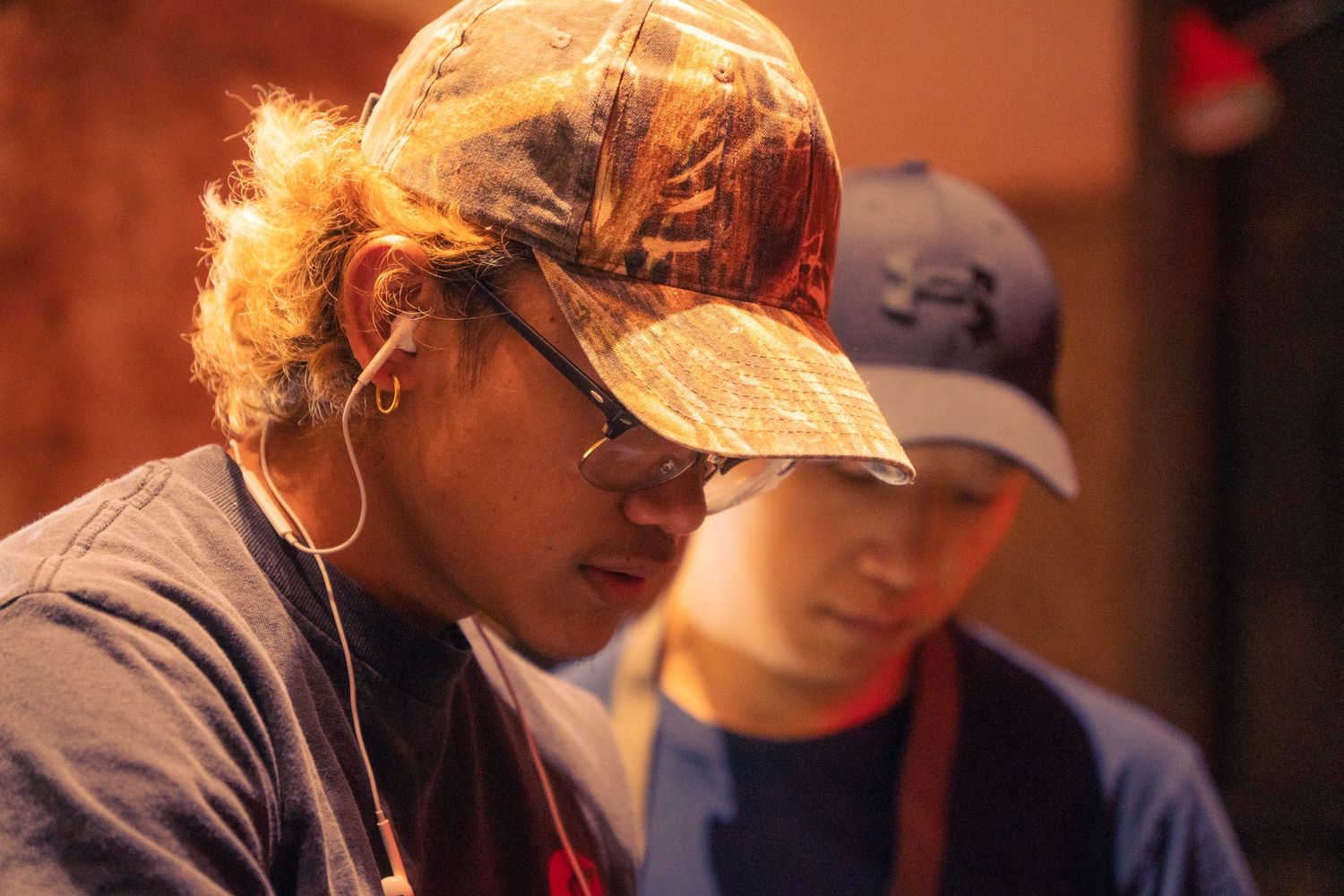 Two people wearing baseball caps under warm golden light on a film set.