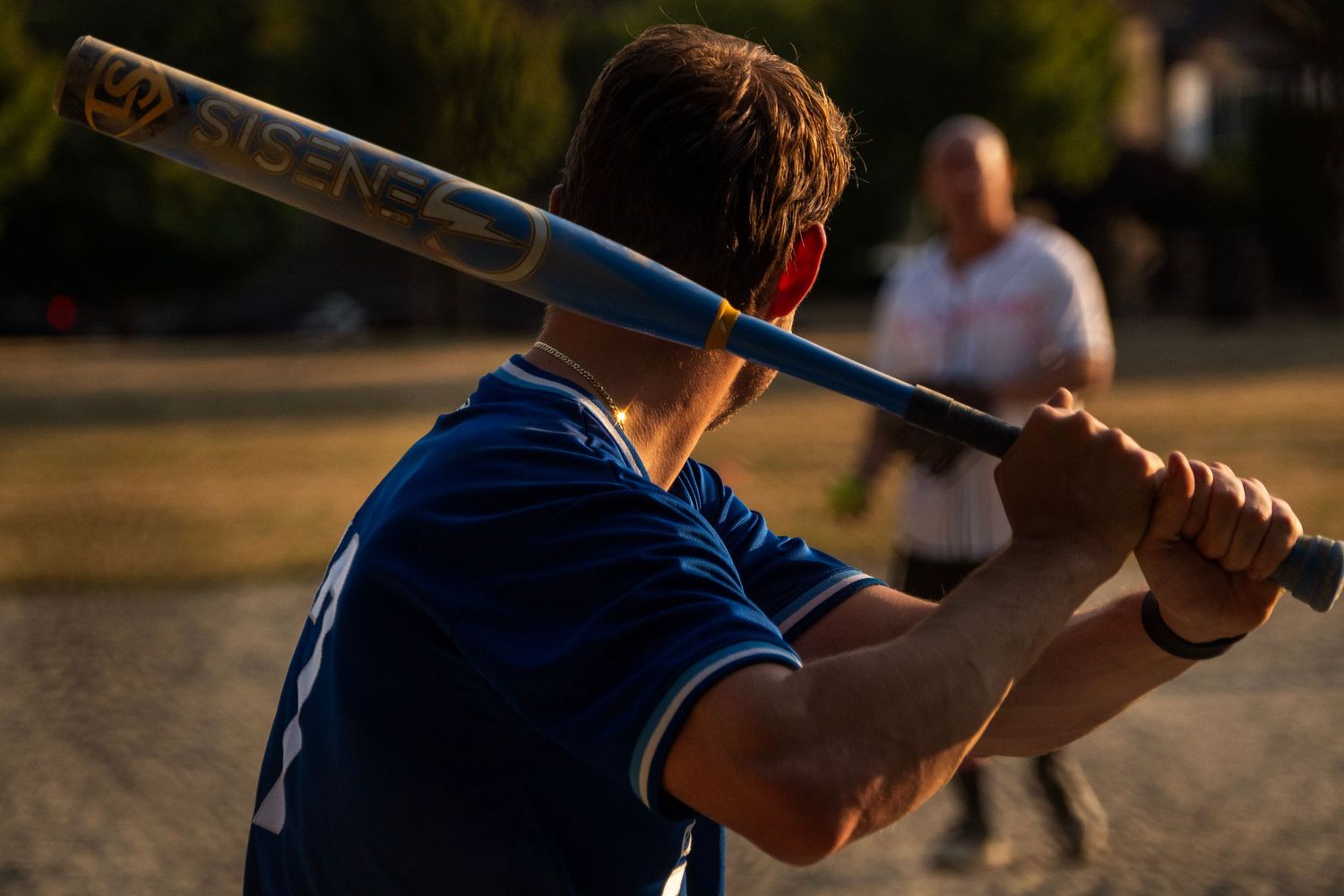 Close-up of a softball batter in a blue jersey holding a DeMarini bat at golden hour.