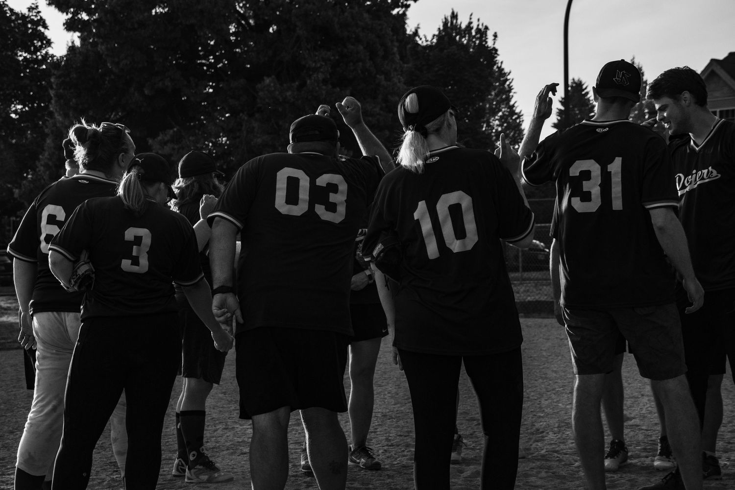 Black and white photo of softball team huddle showing jersey numbers 3, 03, 10, 31.