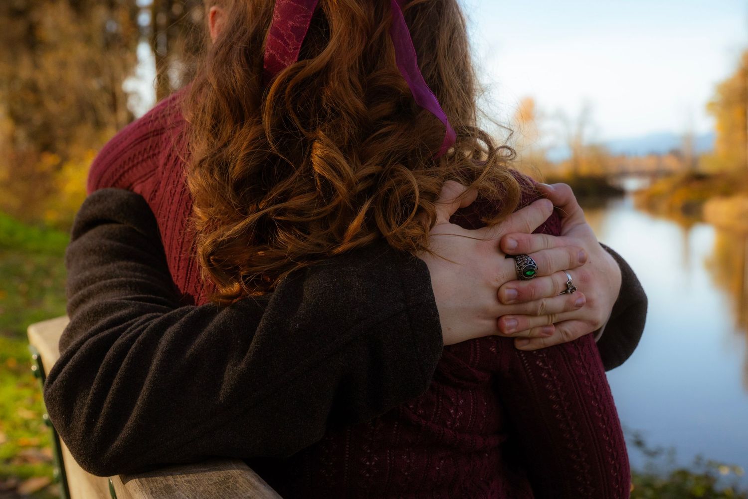 Close-up of couple embracing with intertwined hands near an autumn river, woman wearing a turquoise ring.