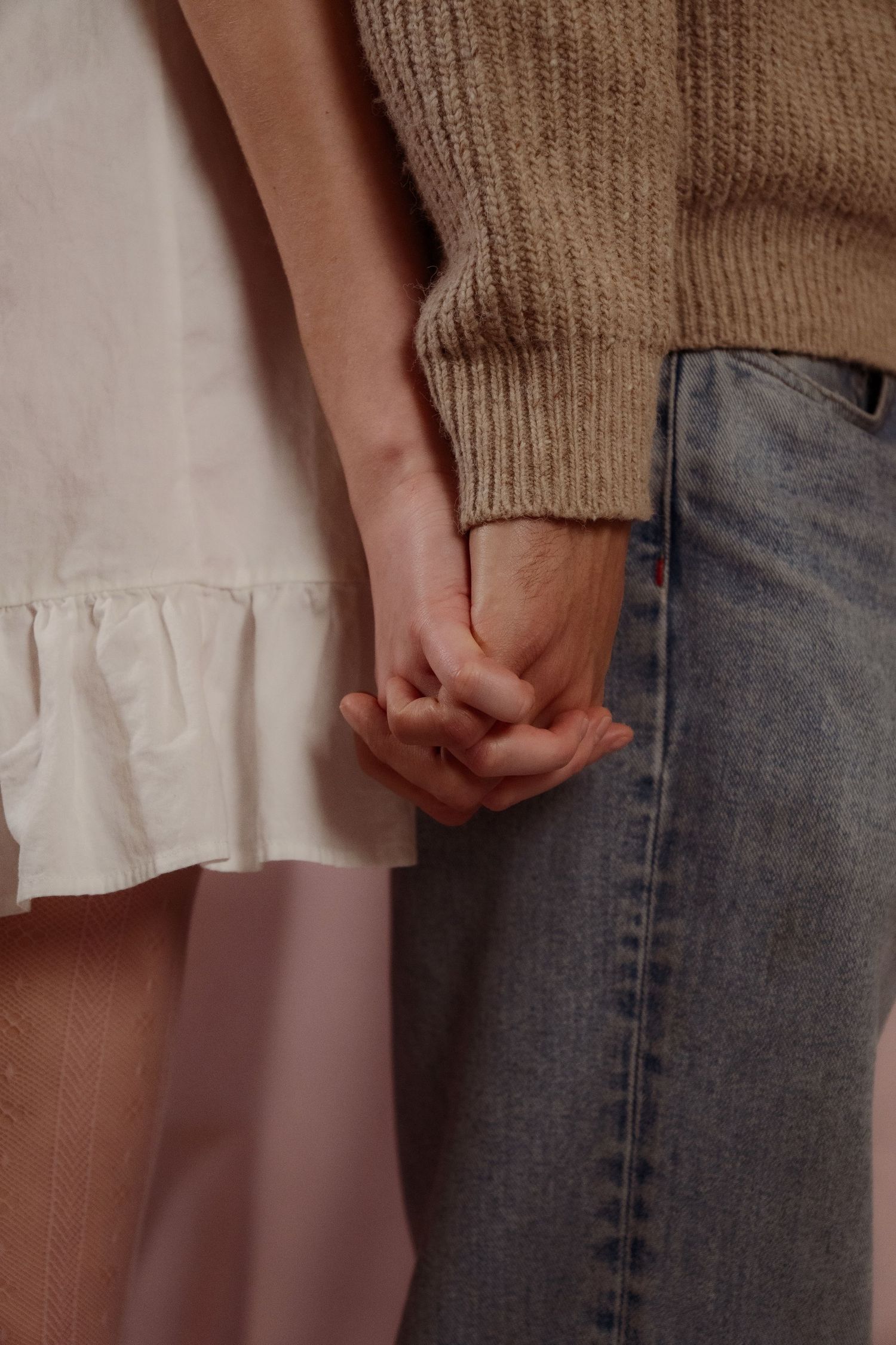 Close-up of a young couple holding hands, woman in white dress and man in beige knit sweater.
