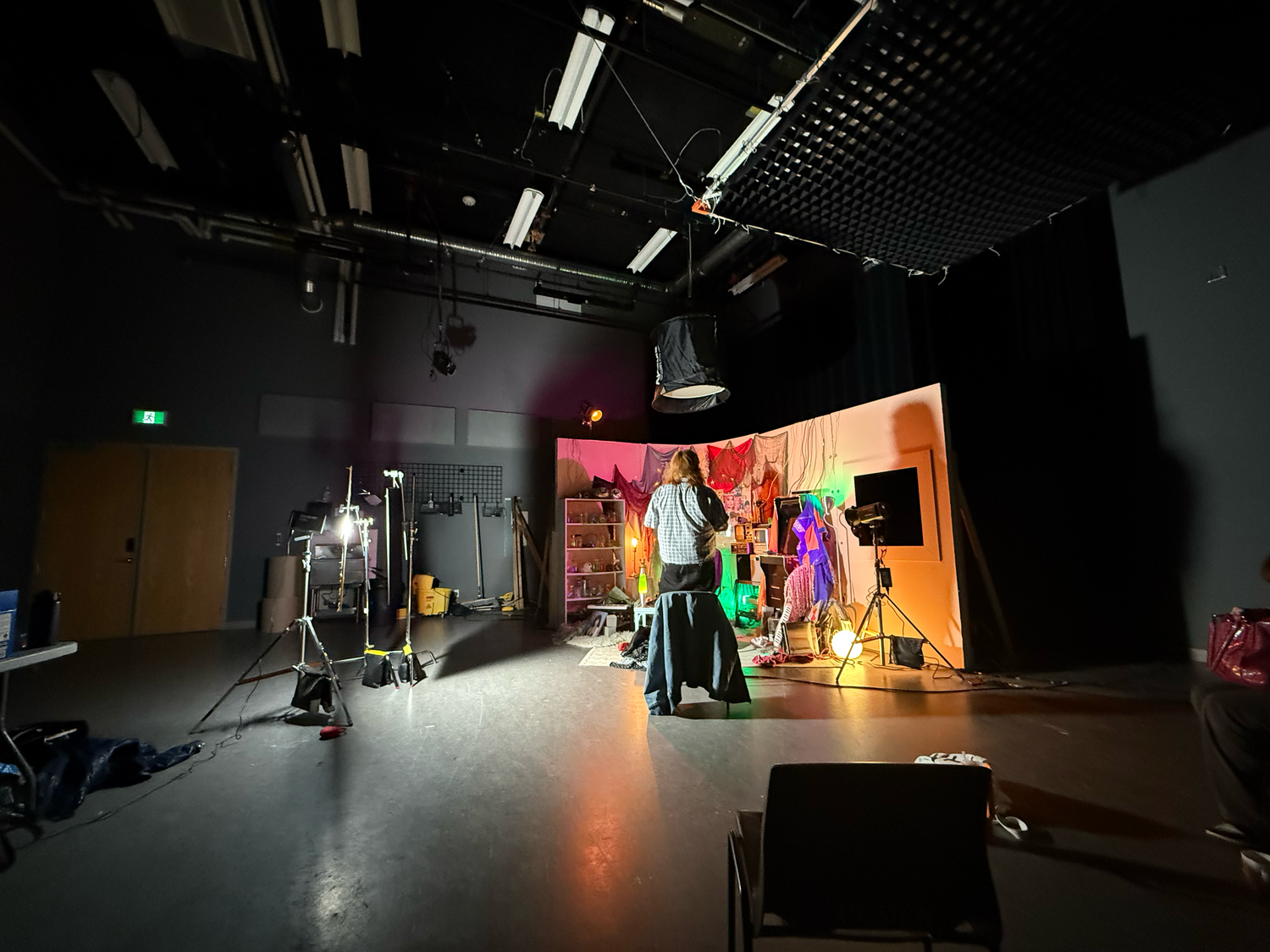 Behind the scenes of a film or photo shoot in a dark studio with colorful set and lighting equipment.