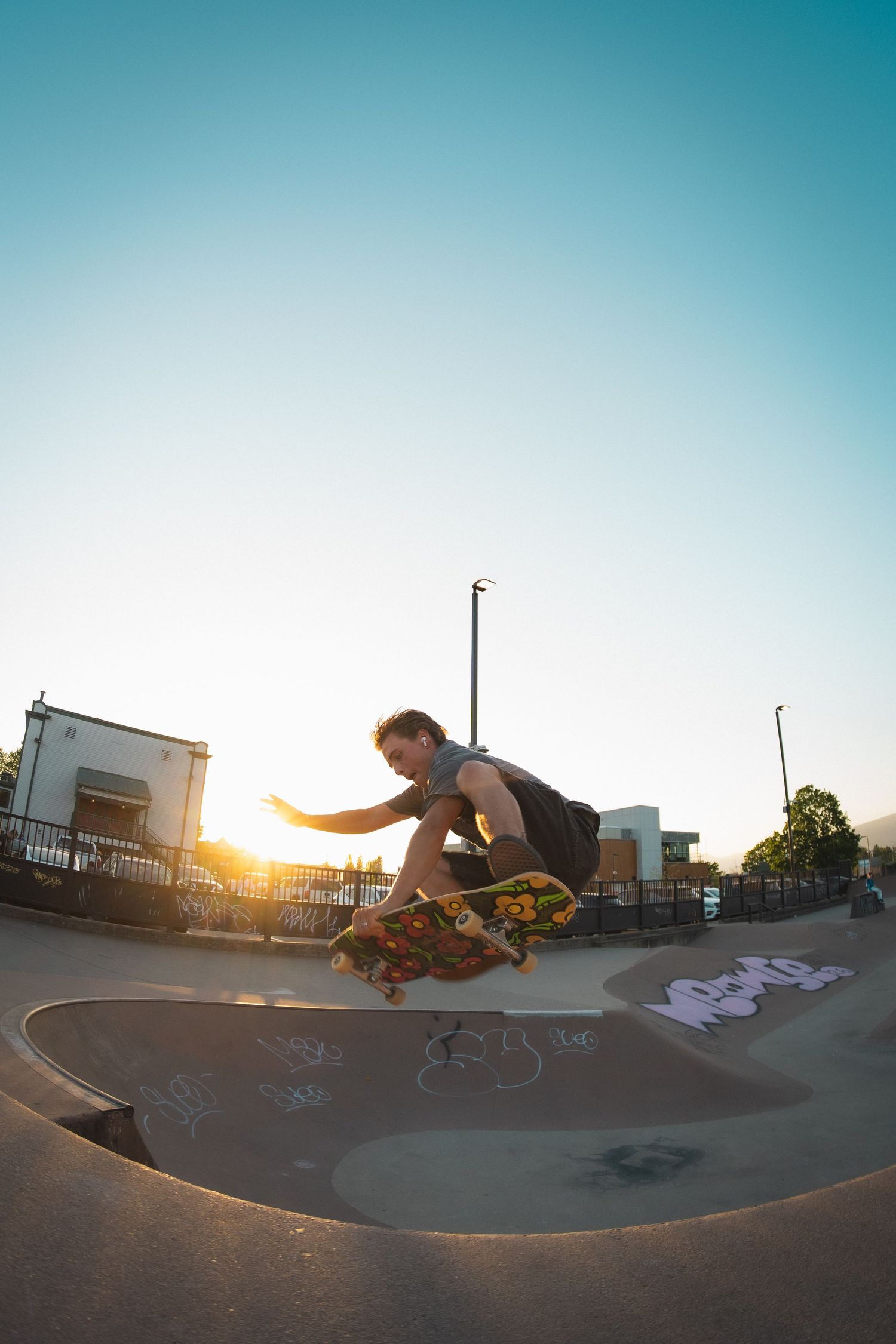 Skateboarder performing a trick at golden hour in a skate park with graffiti-covered ramps.