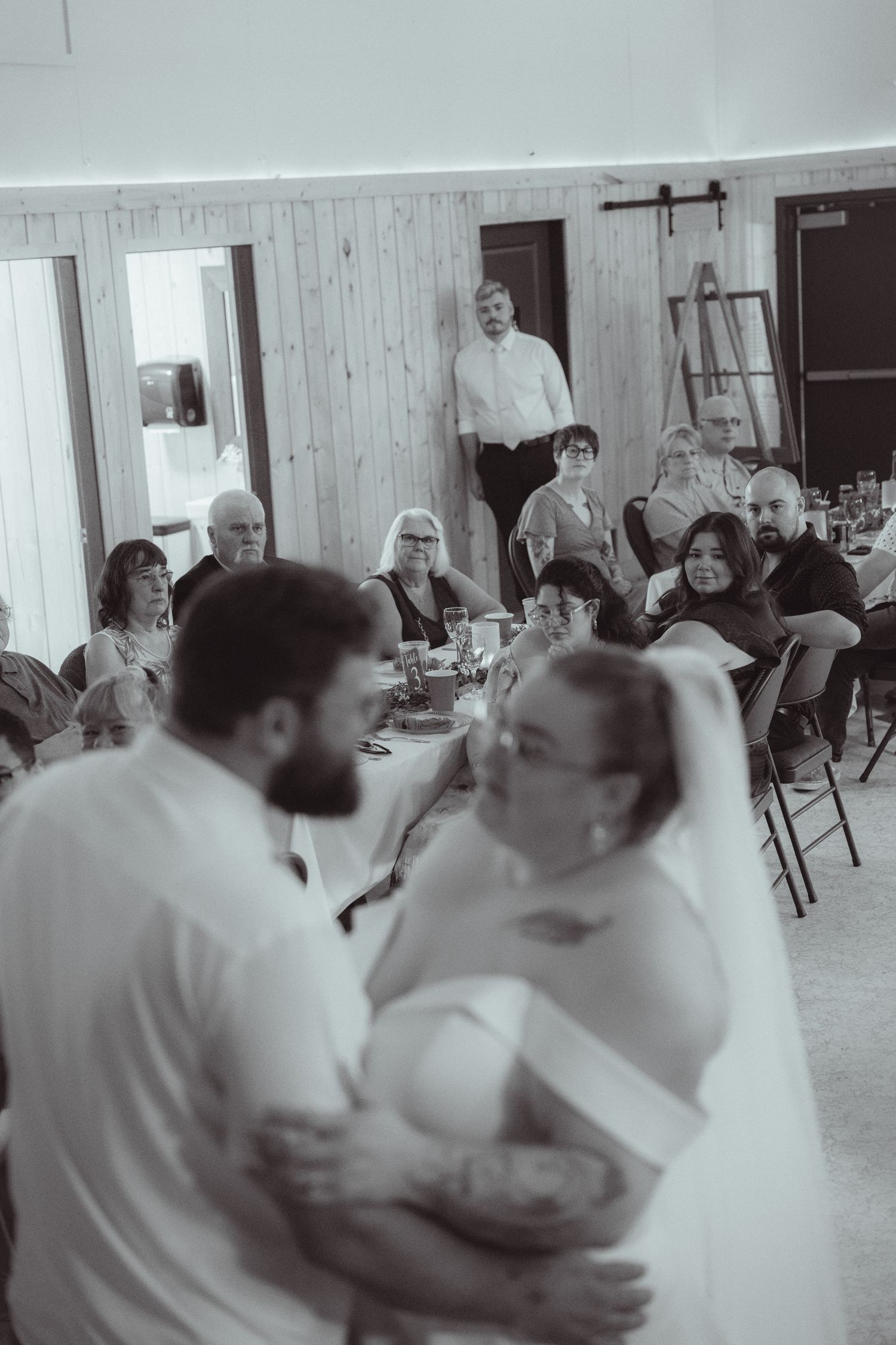 Bride and groom share their first dance as wedding guests watch and celebrate in a rustic barn reception venue.