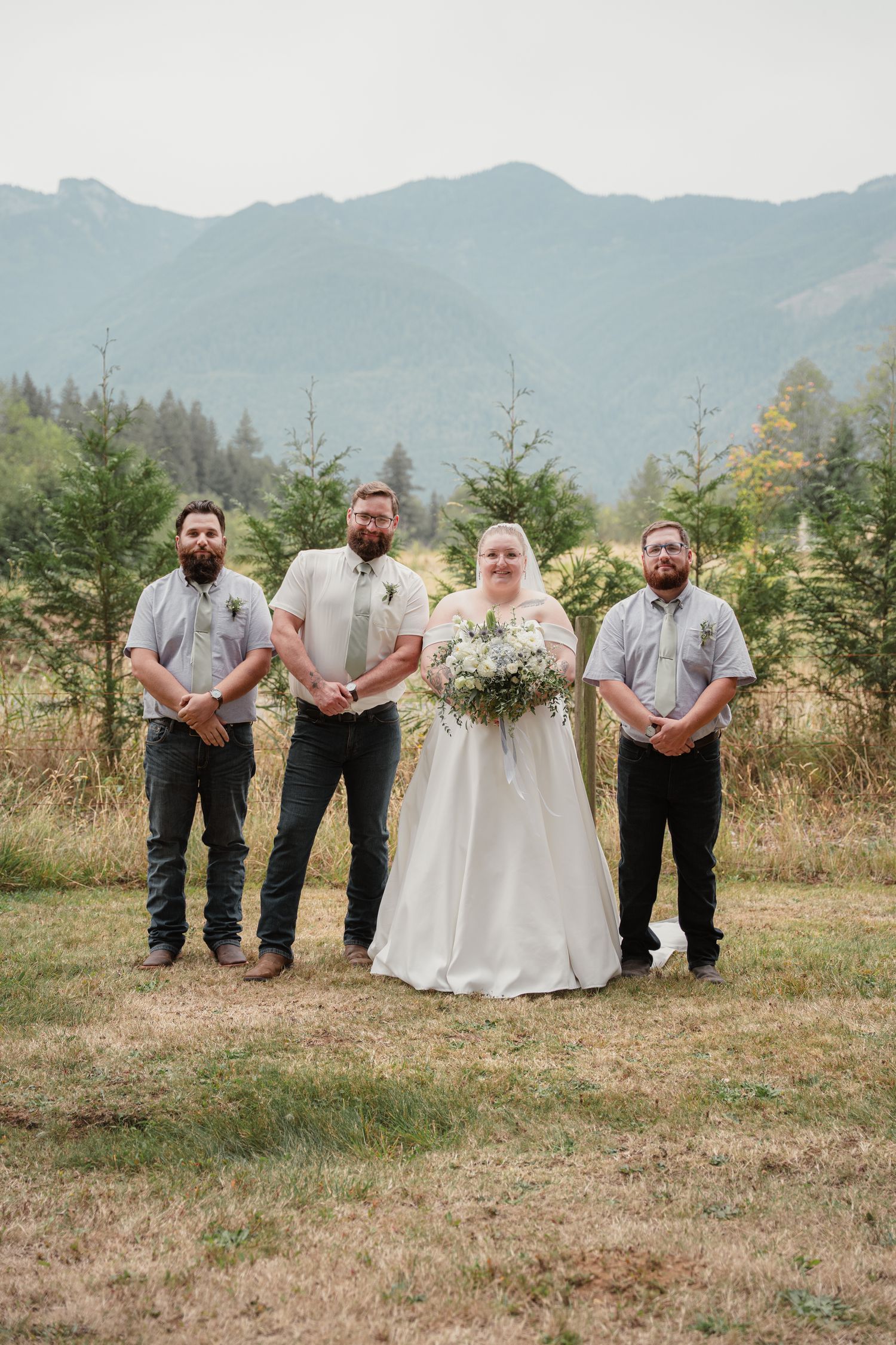 Bride in white gown poses with three groomsmen in matching gray shirts in mountain setting.