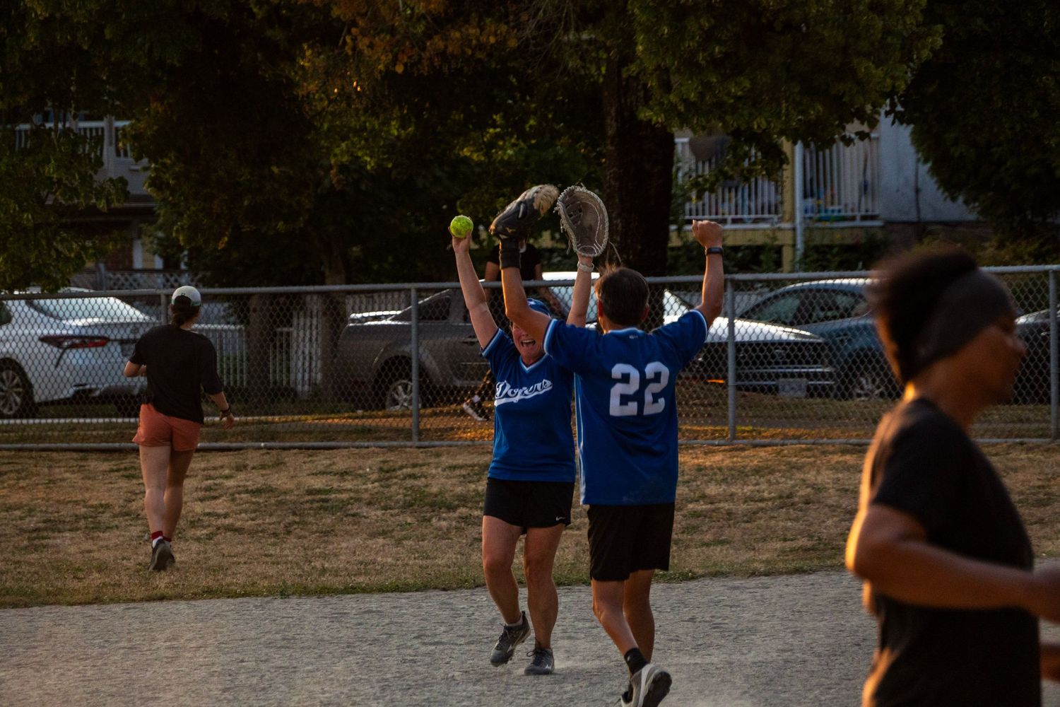 Two softball players in blue Dodgers jerseys catch a ball during an evening game.