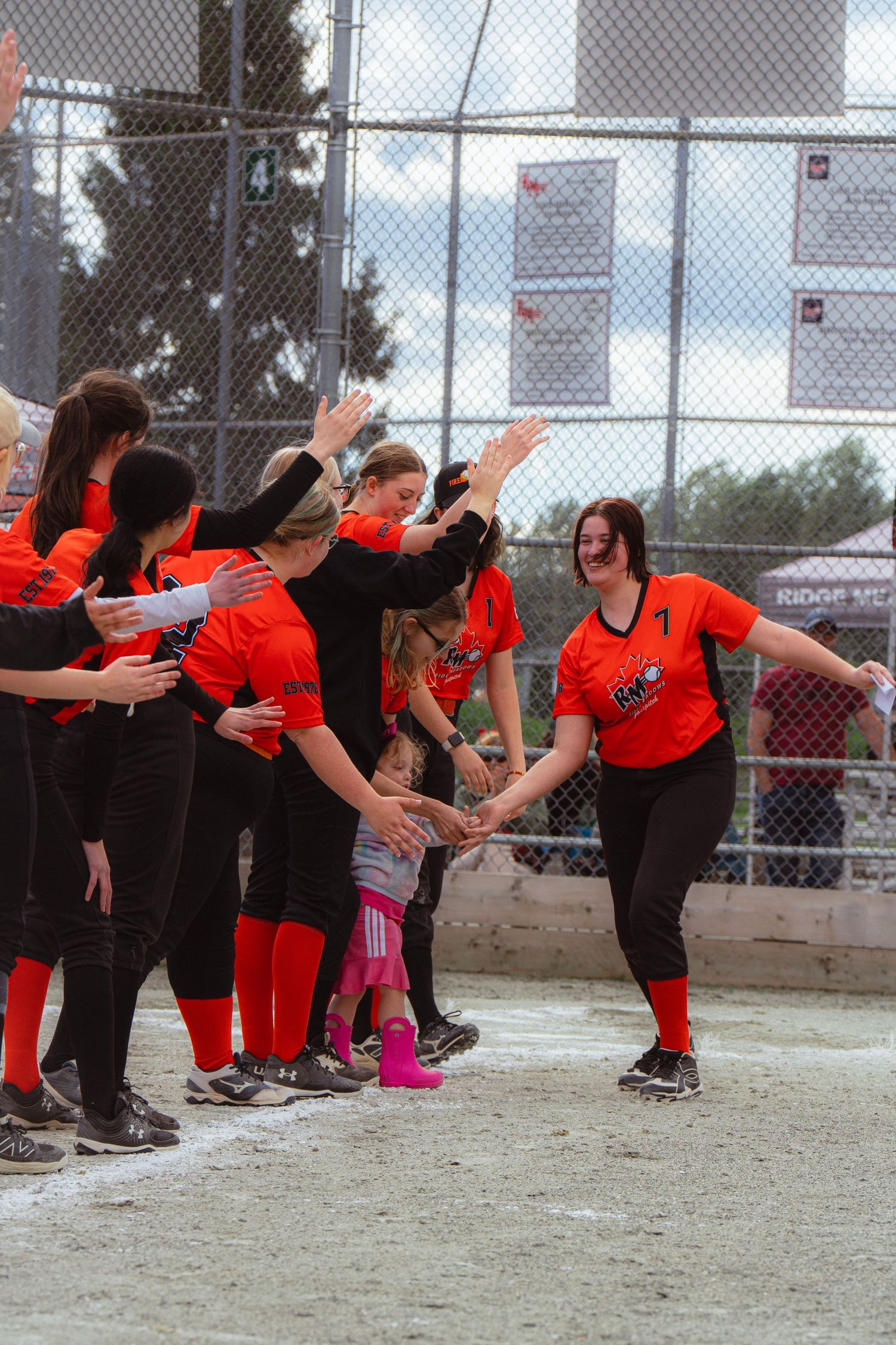 Softball player number 1 in orange uniform receives high-fives from teammates along the baseline.
