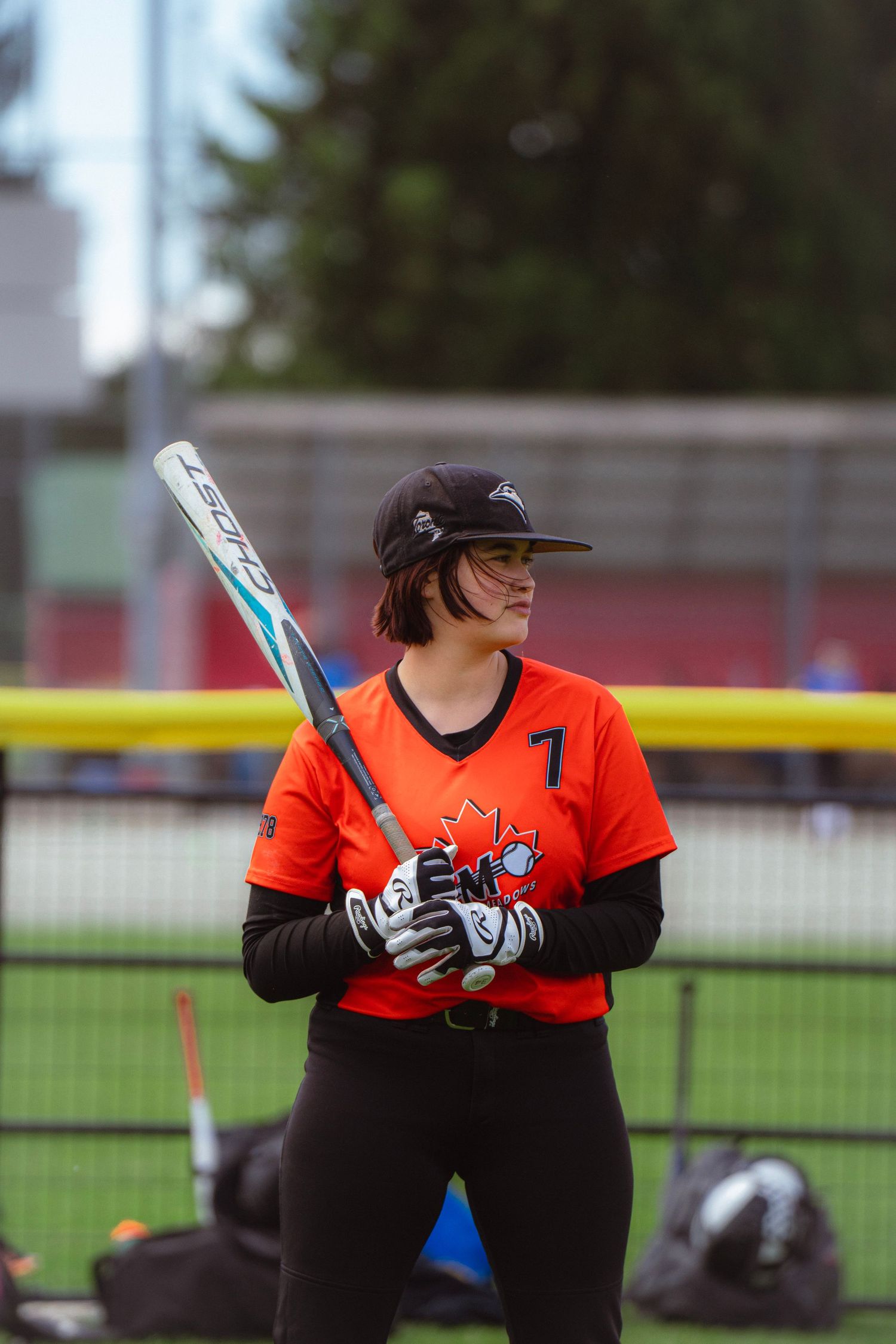 Female softball player #7 in orange jersey holding bat on field.