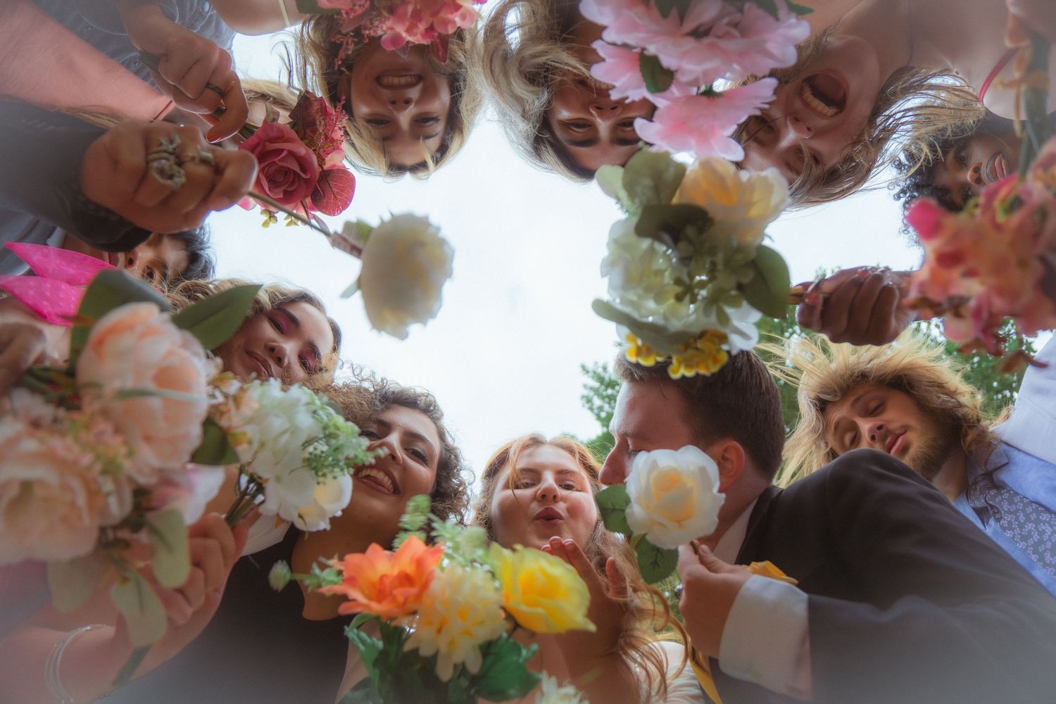 Upward view of wedding party huddle holding vibrant pink orange and white flower bouquets.