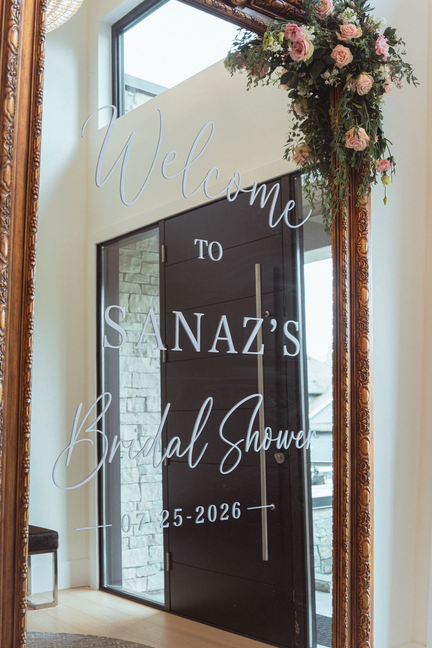 Elegant bridal shower welcome sign in gold mirror frame with floral arrangement, reading Welcome to Sanaz's Bridal Shower 07-25-2026.