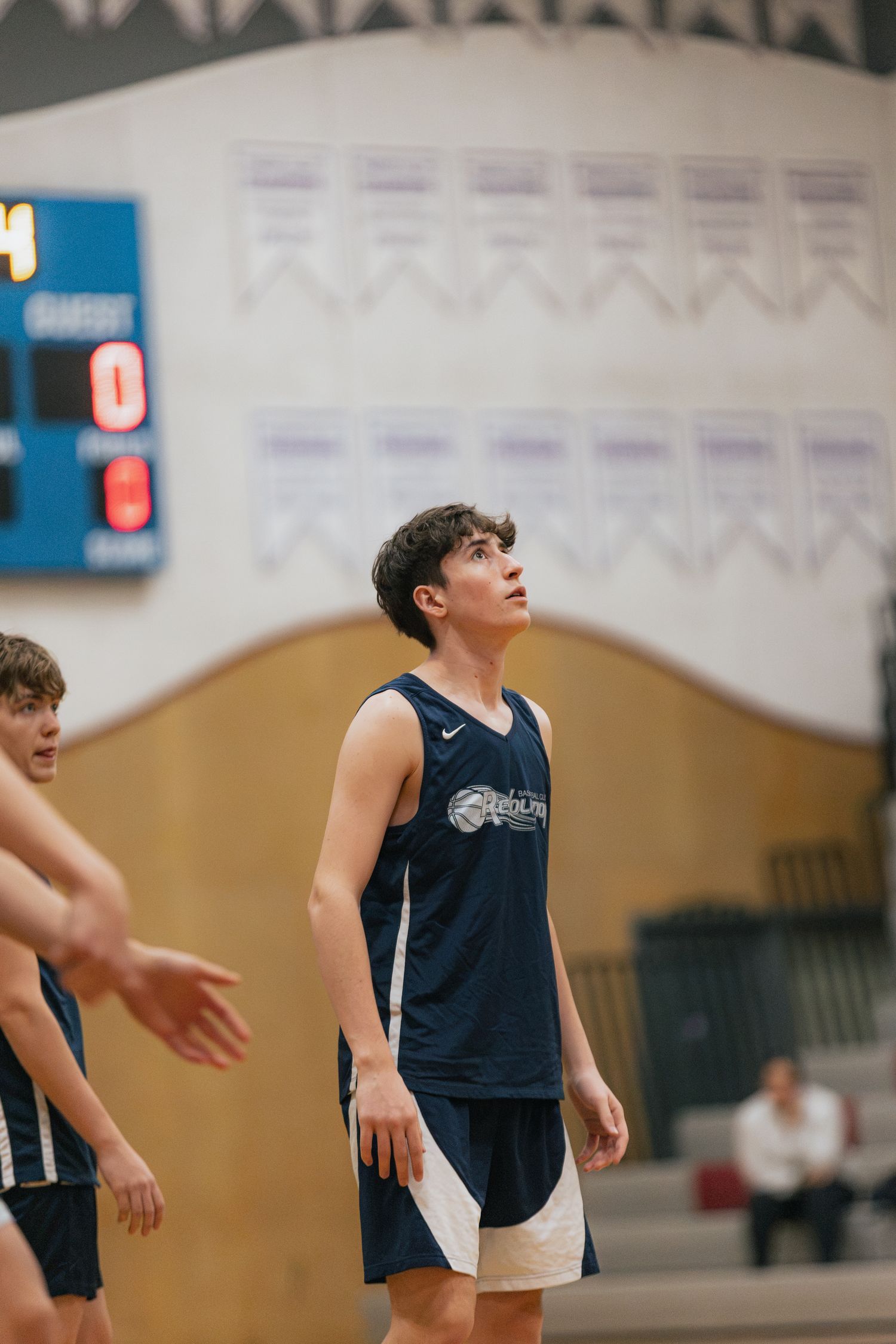 A young male basketball player in a navy Nike jersey looks up during an indoor gymnasium game.