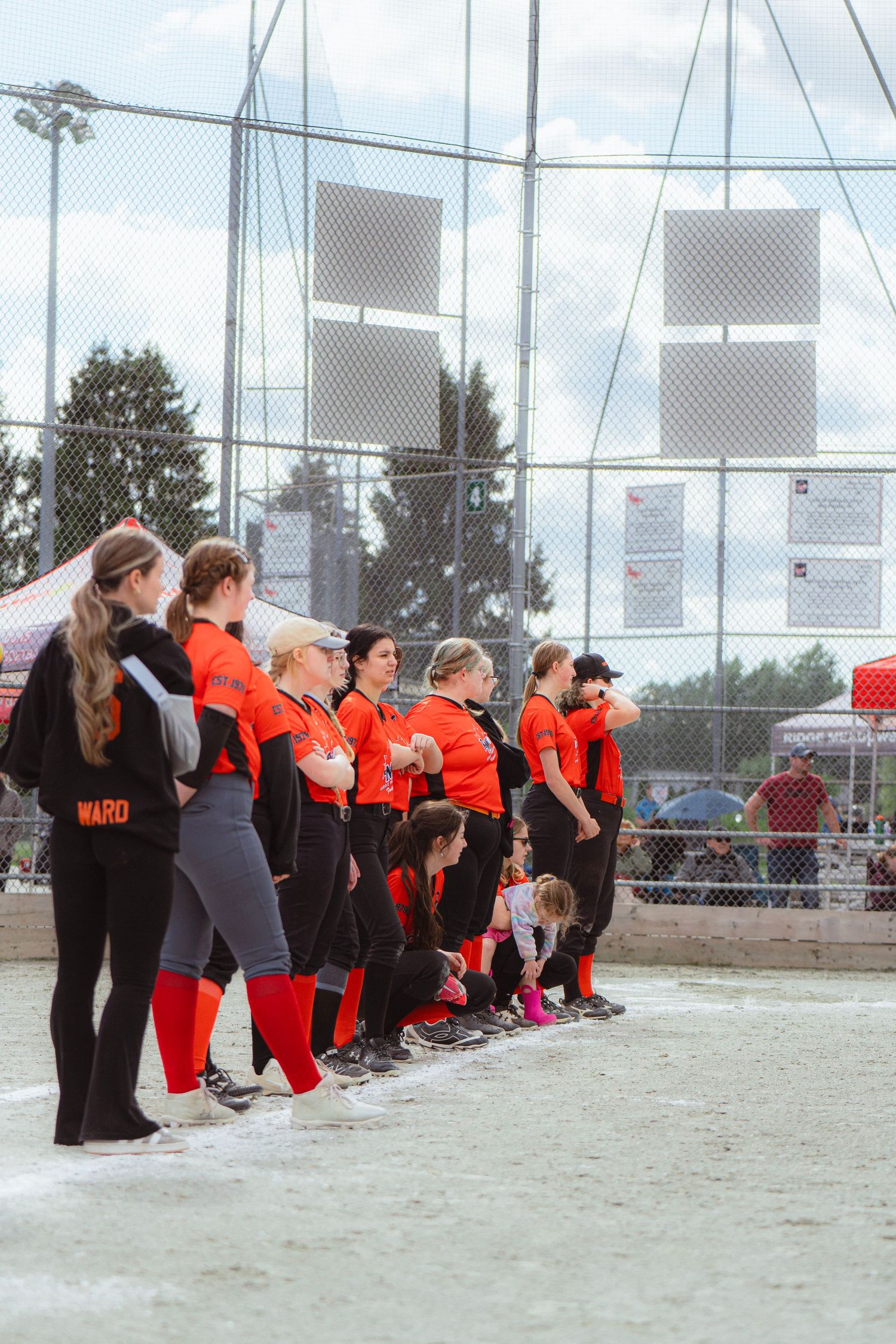 Female softball team in orange and black uniforms lined up along baseline after game.