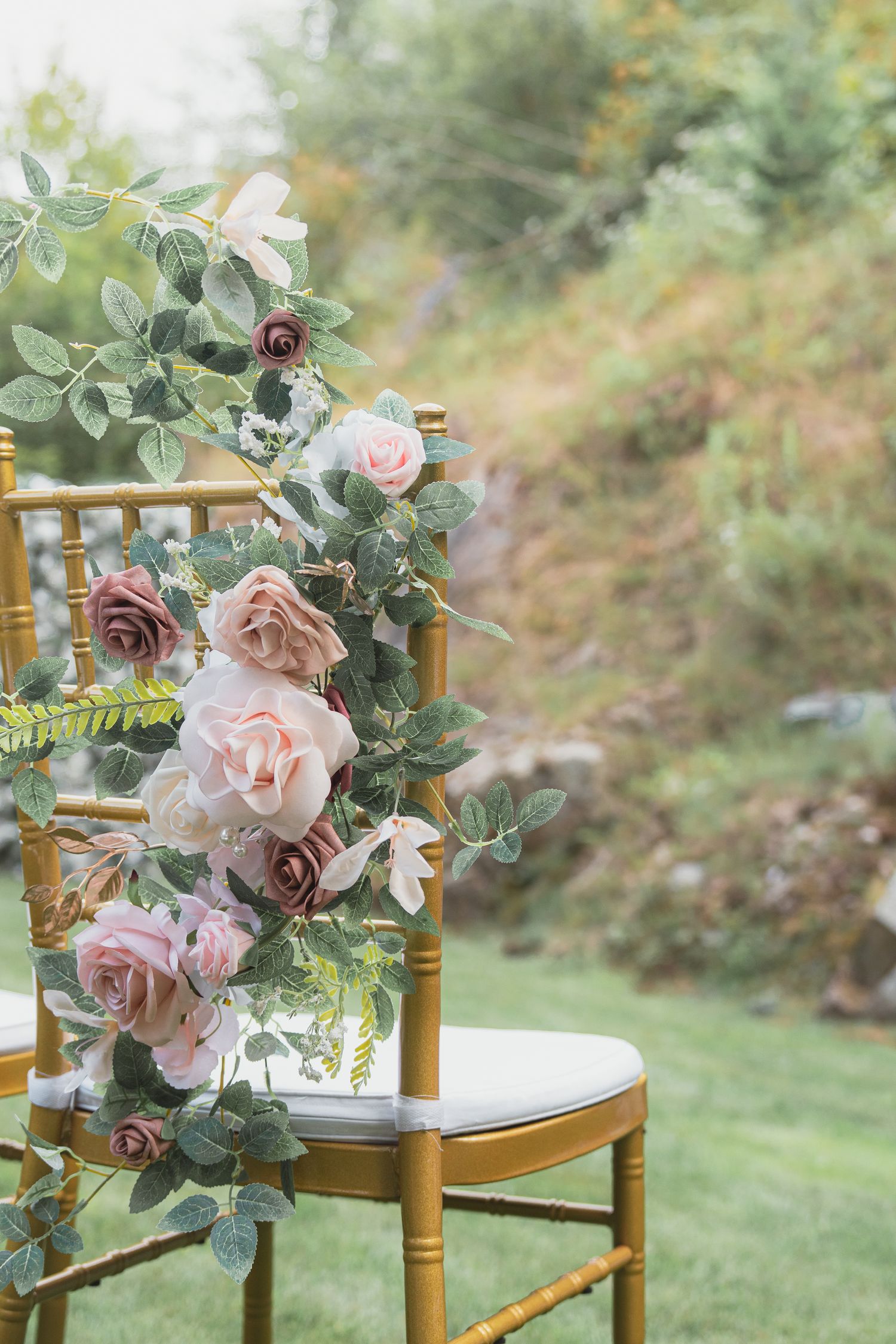 Gold chiavari chair decorated with blush pink and mauve roses with eucalyptus greenery at an outdoor wedding ceremony.