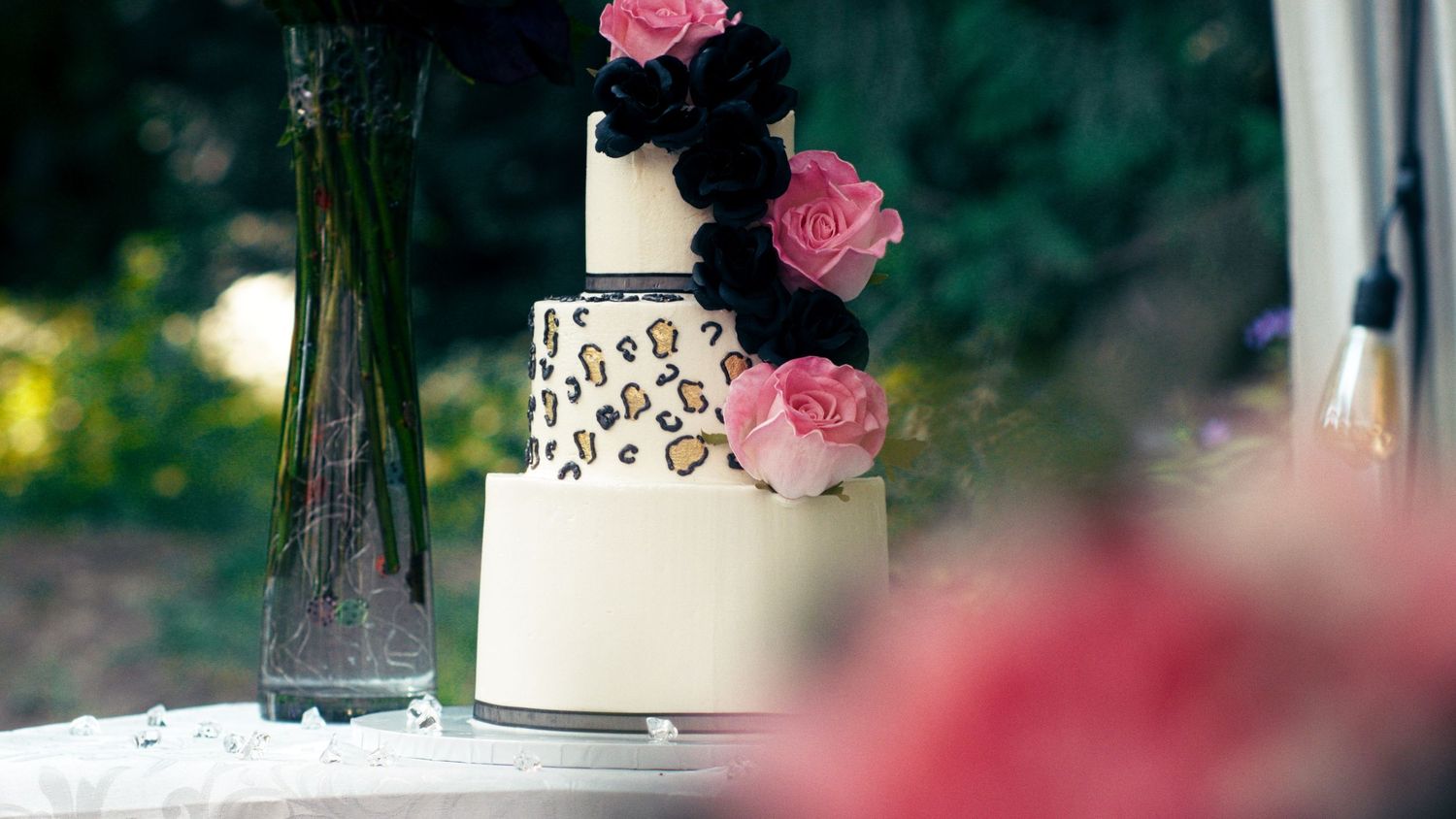 Three-tier wedding cake with leopard print and black and pink floral decorations displayed outdoors.