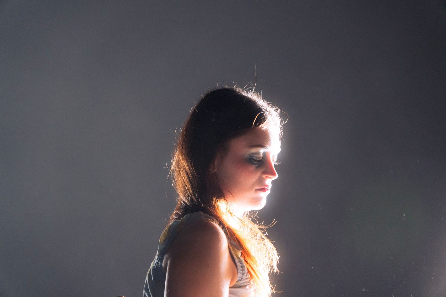 Portrait of a young woman with long hair lit by warm side light against a dark gray background.