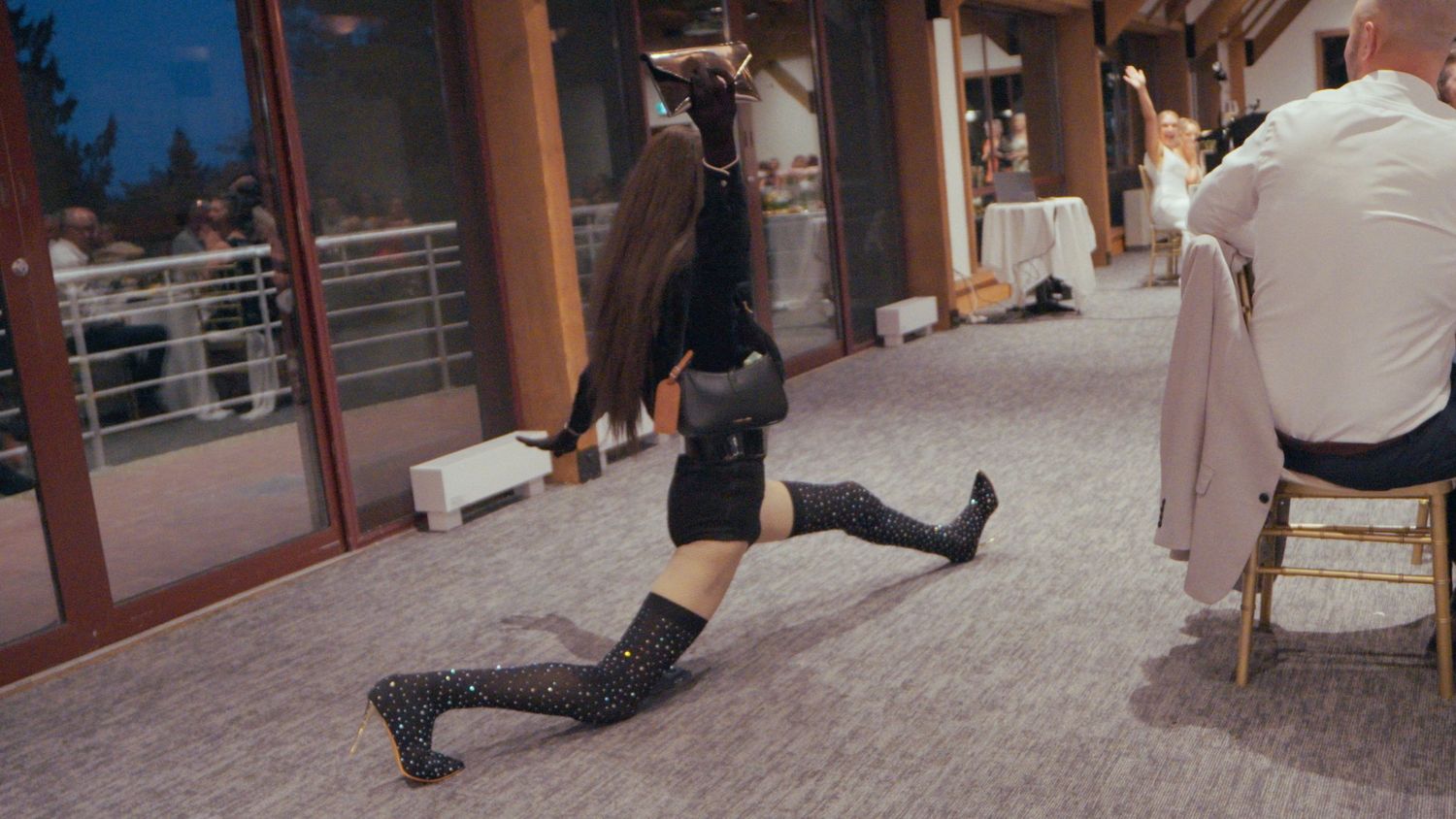 A dancer in black outfit and sequined stockings performs a floor split at an outdoor wedding event.