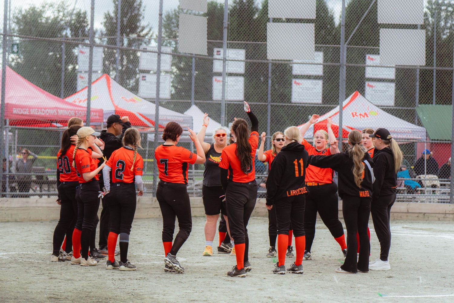 Female softball team in orange uniforms celebrating together on the field after win.