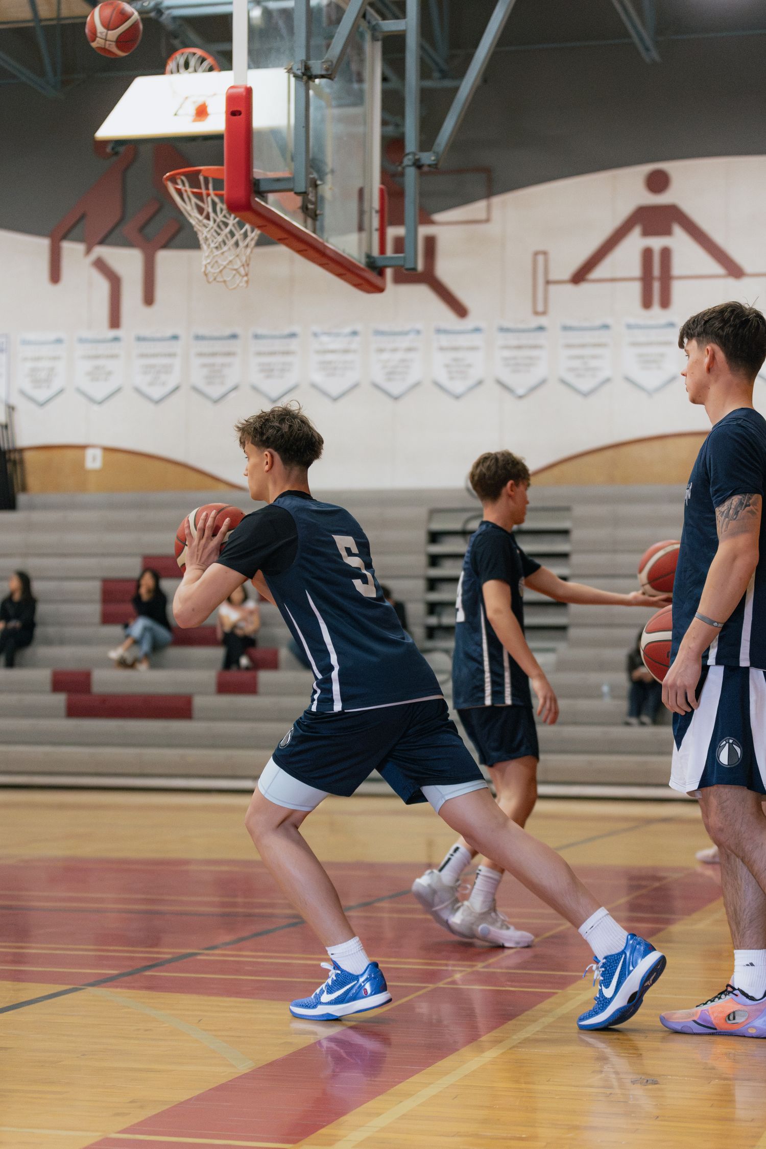 Youth basketball players in navy uniforms practice passing and dribbling drills in a school gym.