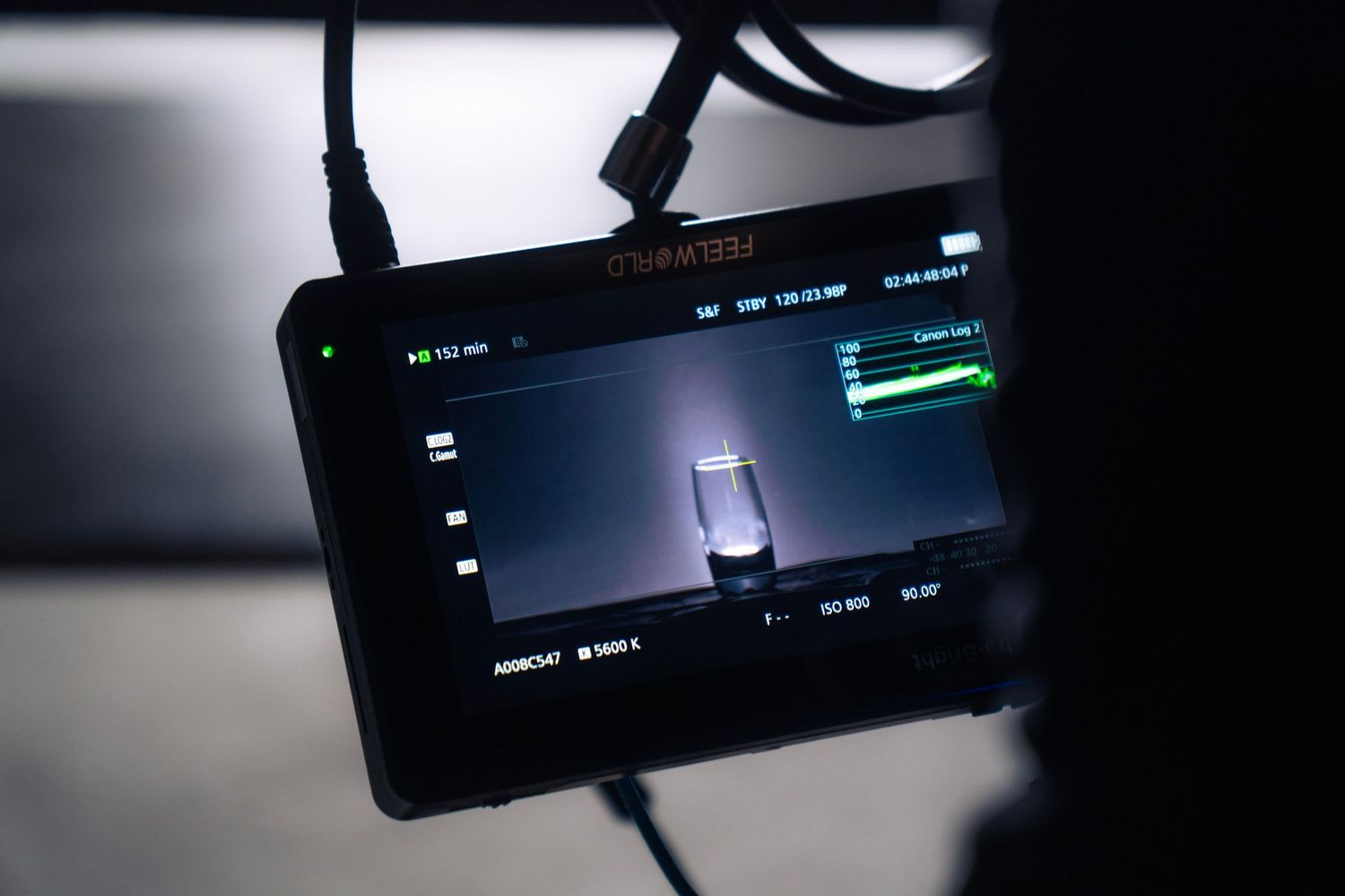 Camera monitor displaying a glass of liquid being filmed in a dark professional studio setup.
