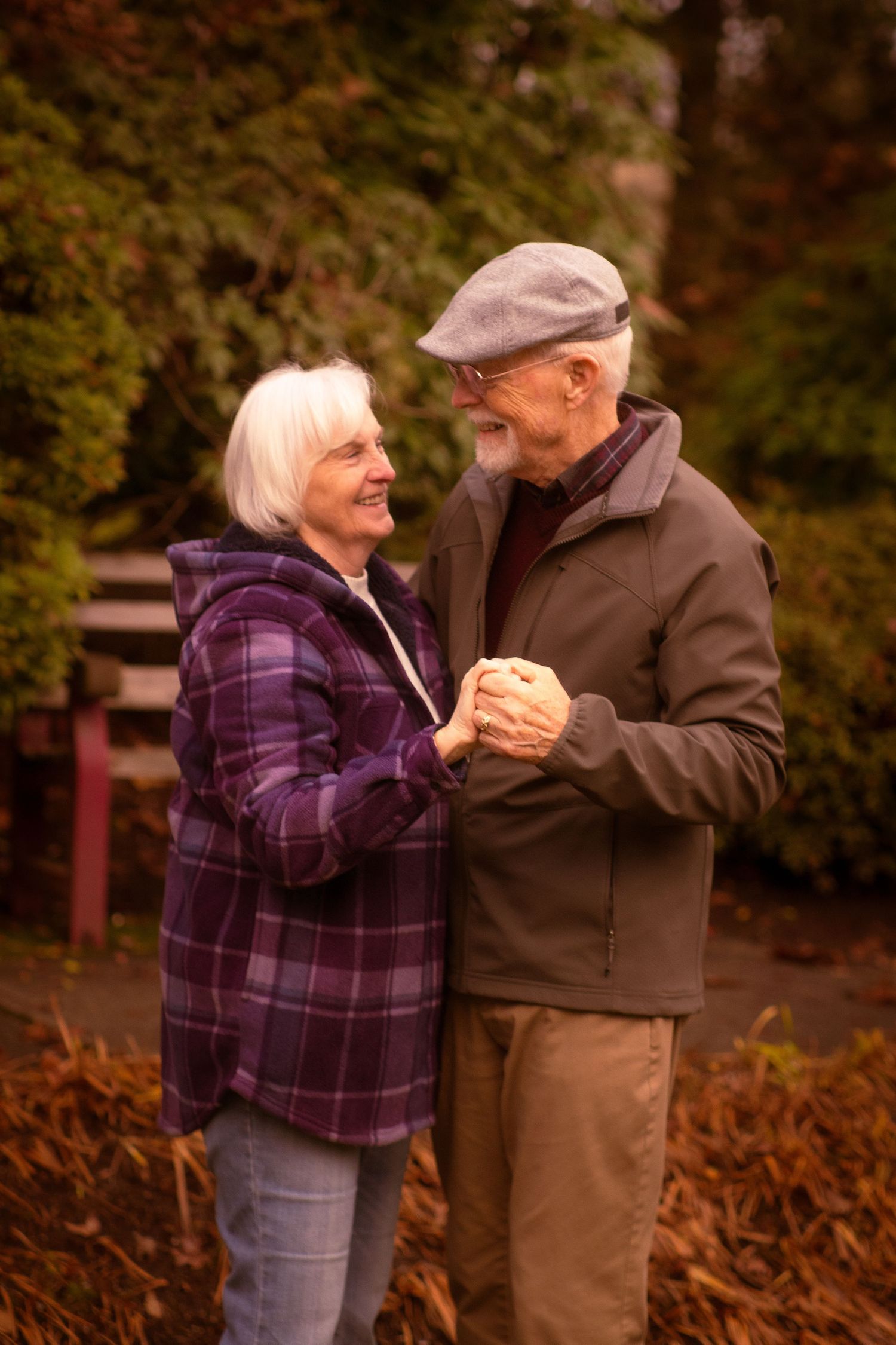 Older couple dancing together outdoors, holding hands and smiling in an autumn park.