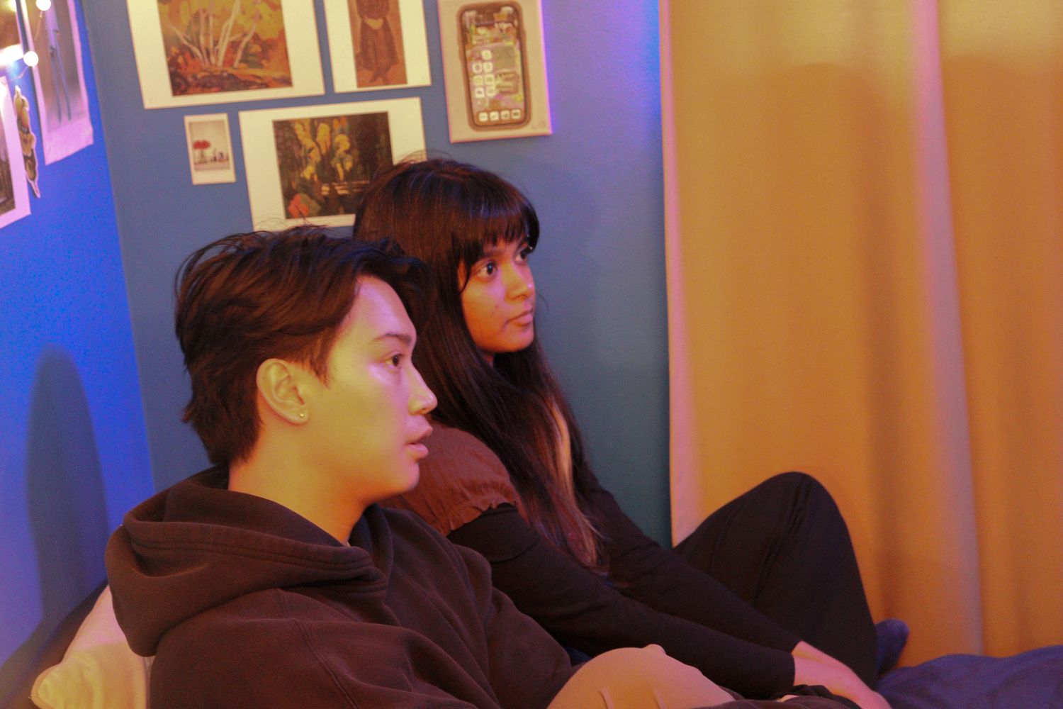 Two actors sitting against a colorful wall during a film production scene.