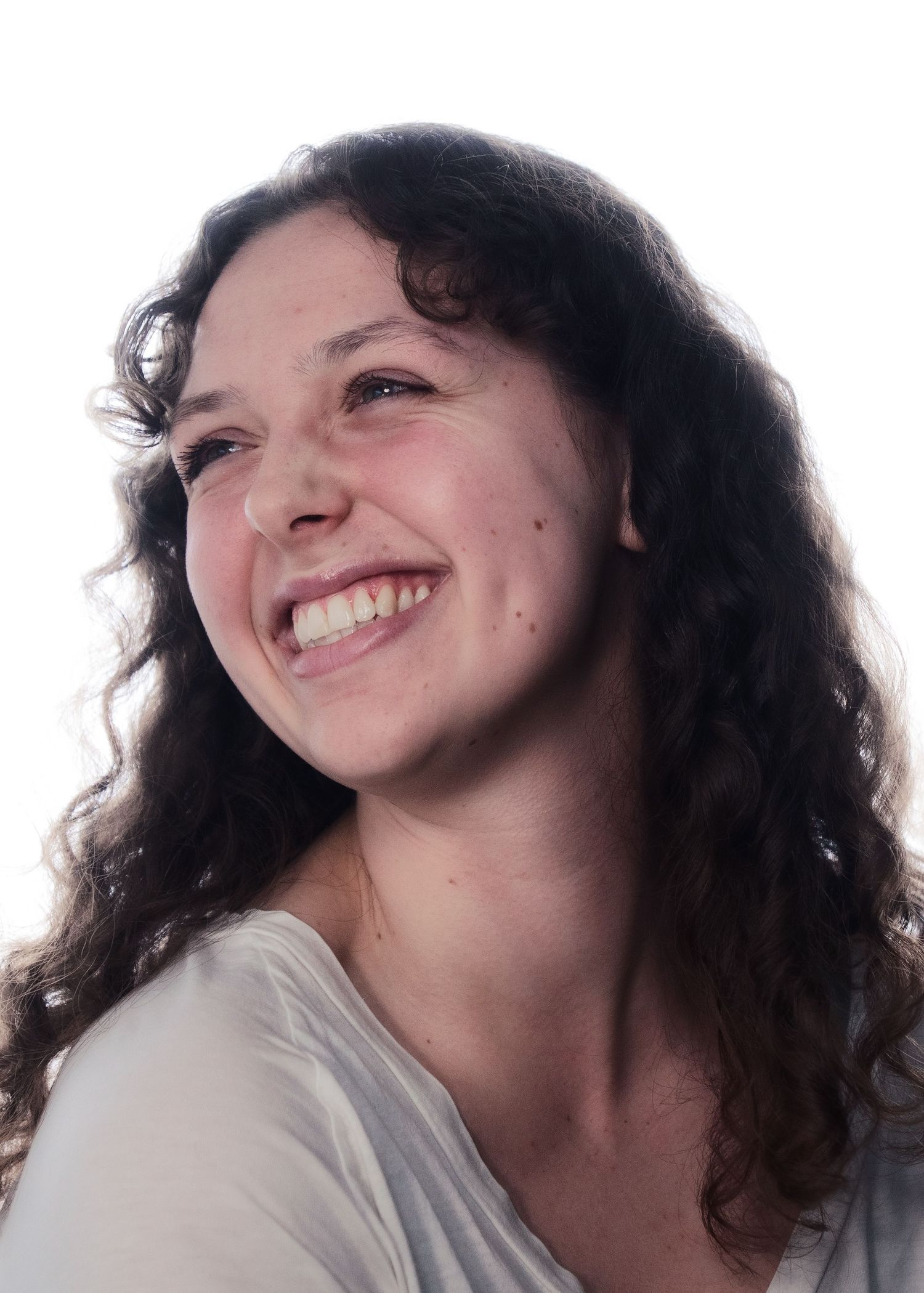 Young woman with curly dark hair laughing joyfully while looking up against a bright background.